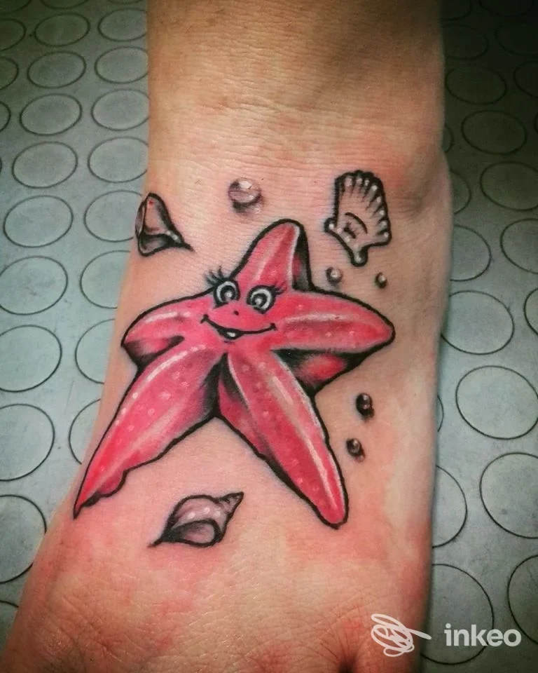 Tatuaggio colorato di una stella marina sorridente sul dorso del piede, circondata da conchiglie e bolle; lavoro realizzato da Sweet Pain Tattoo a Santo Stefano di Magra.