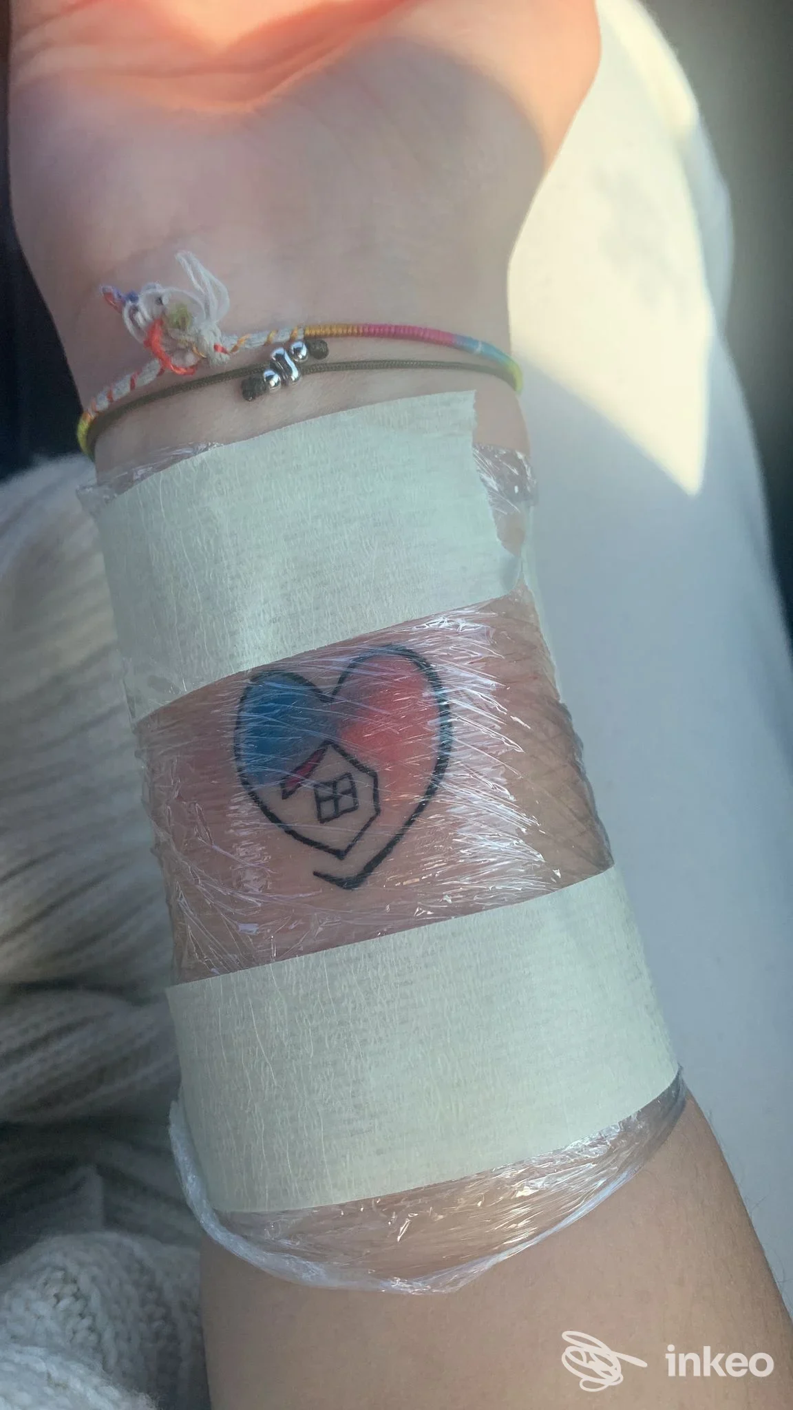 Primo piano di un piccolo tatuaggio cuore con una casetta sul polso, avvolto in pellicola dopo la sessione. Sweet Pain Tattoo, Santo Stefano di Magra.
