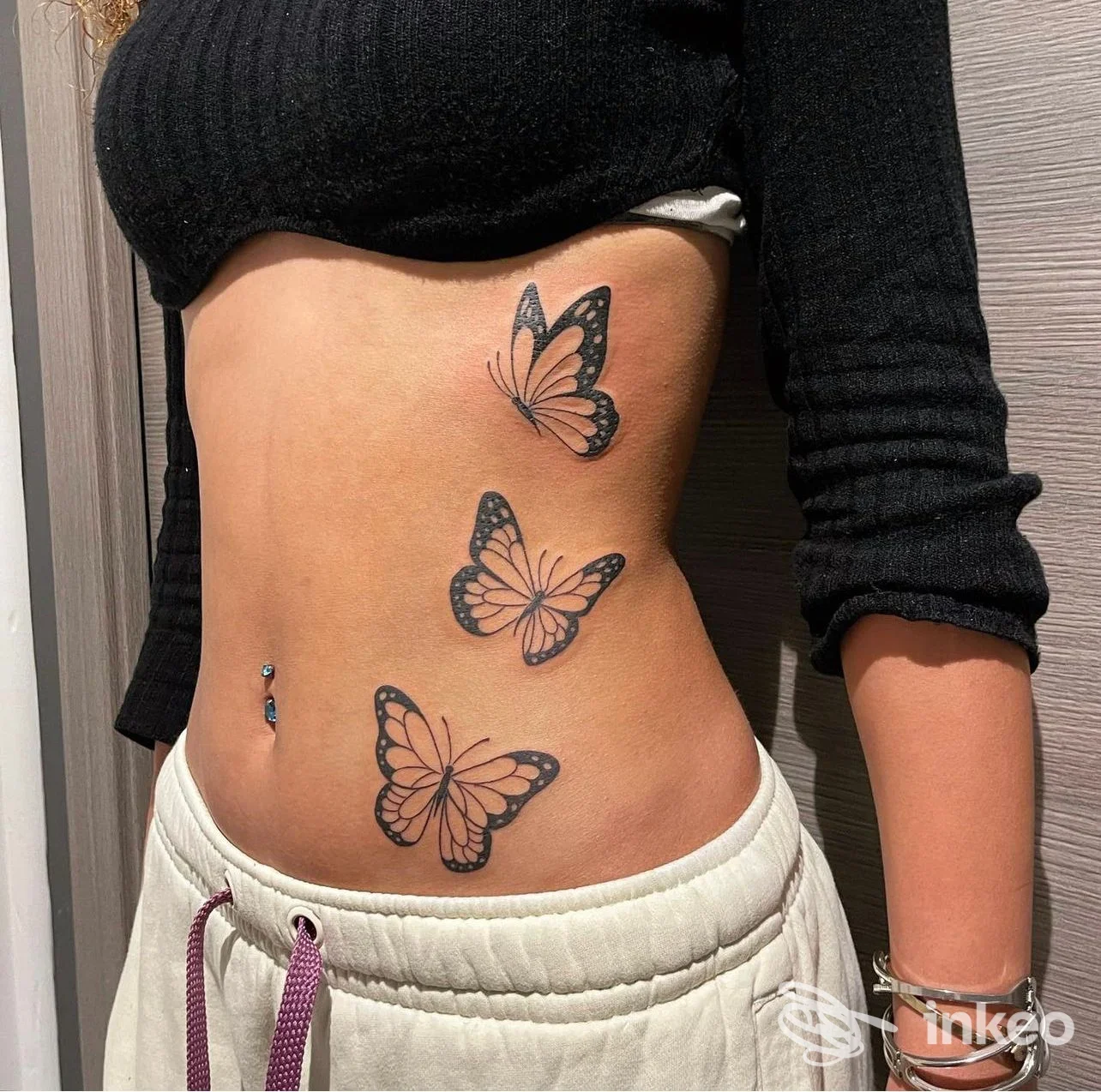 Tre farfalle tatuate sul fianco destro di una persona con piercing ombelicale; immagine per Tattoo & Piercing White Moon, Imperia.