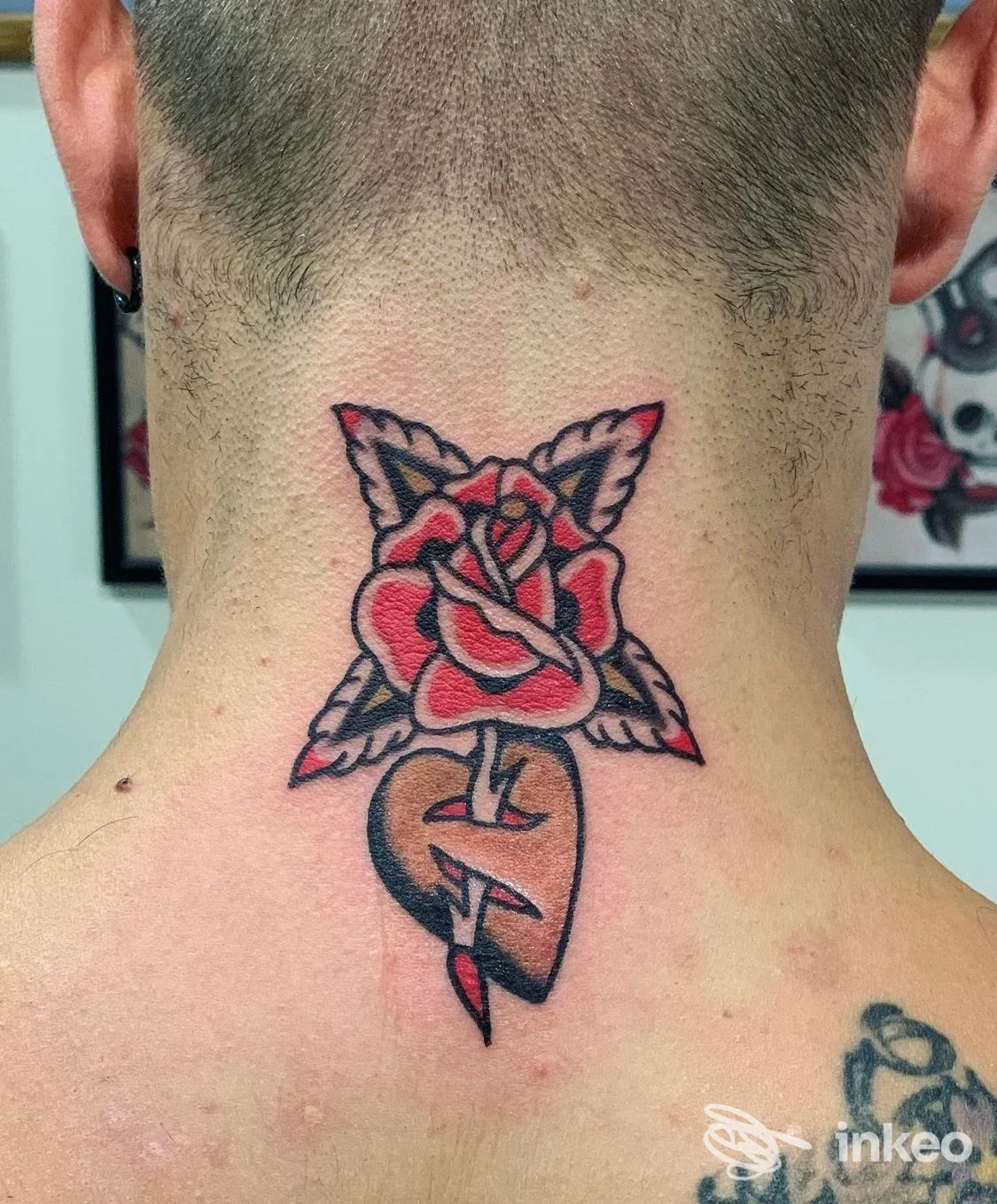 Tatuaggio tradizionale di una rosa rossa sopra un cuore trafitto sulla nuca, eseguito da Yuri Nani Tattooing a Varazze; dettaglio su pelle rasata.
