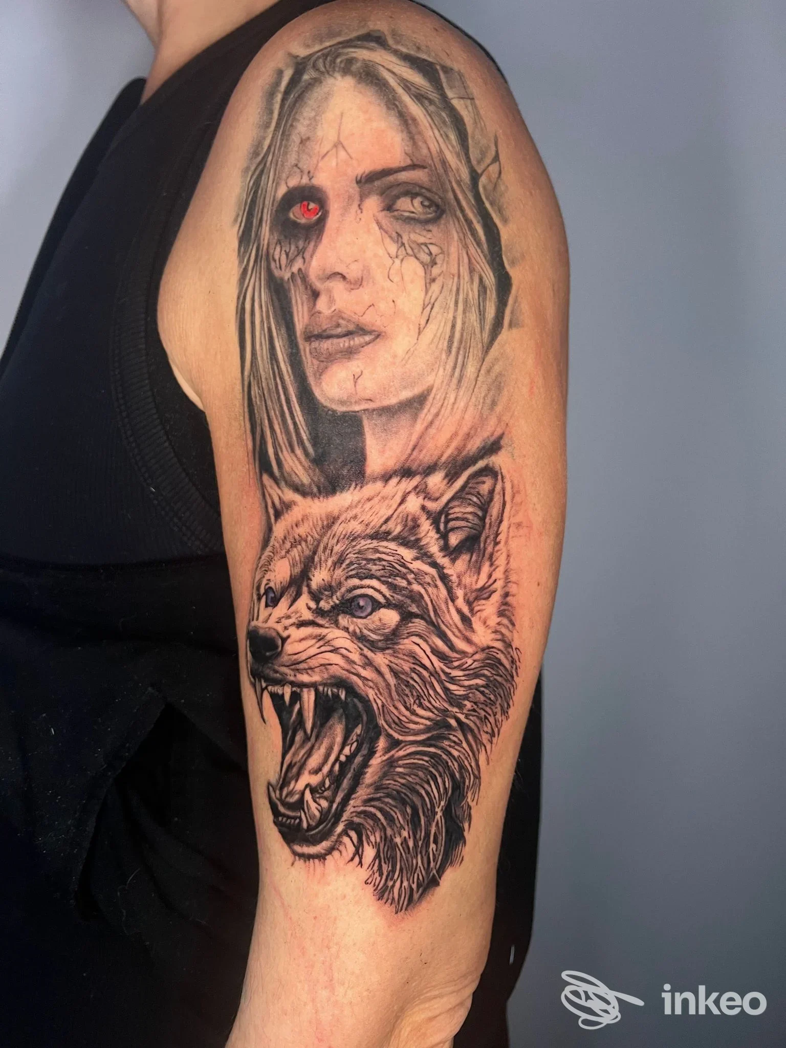 Tatuaggio sul braccio raffigurante una testa di lupo sbavante e una figura femminile con un occhio rosso, eseguito realisticamente sulla pelle.