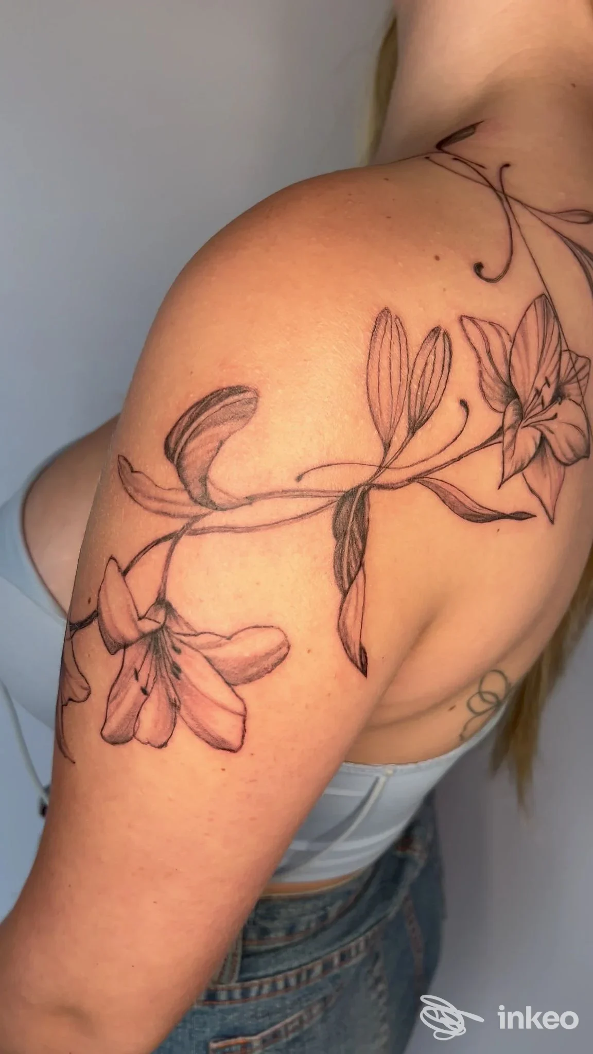 Tattoo floreale lungo la spalla e il braccio, disegno di fiori e rami su pelle reale, senza viso visibile.