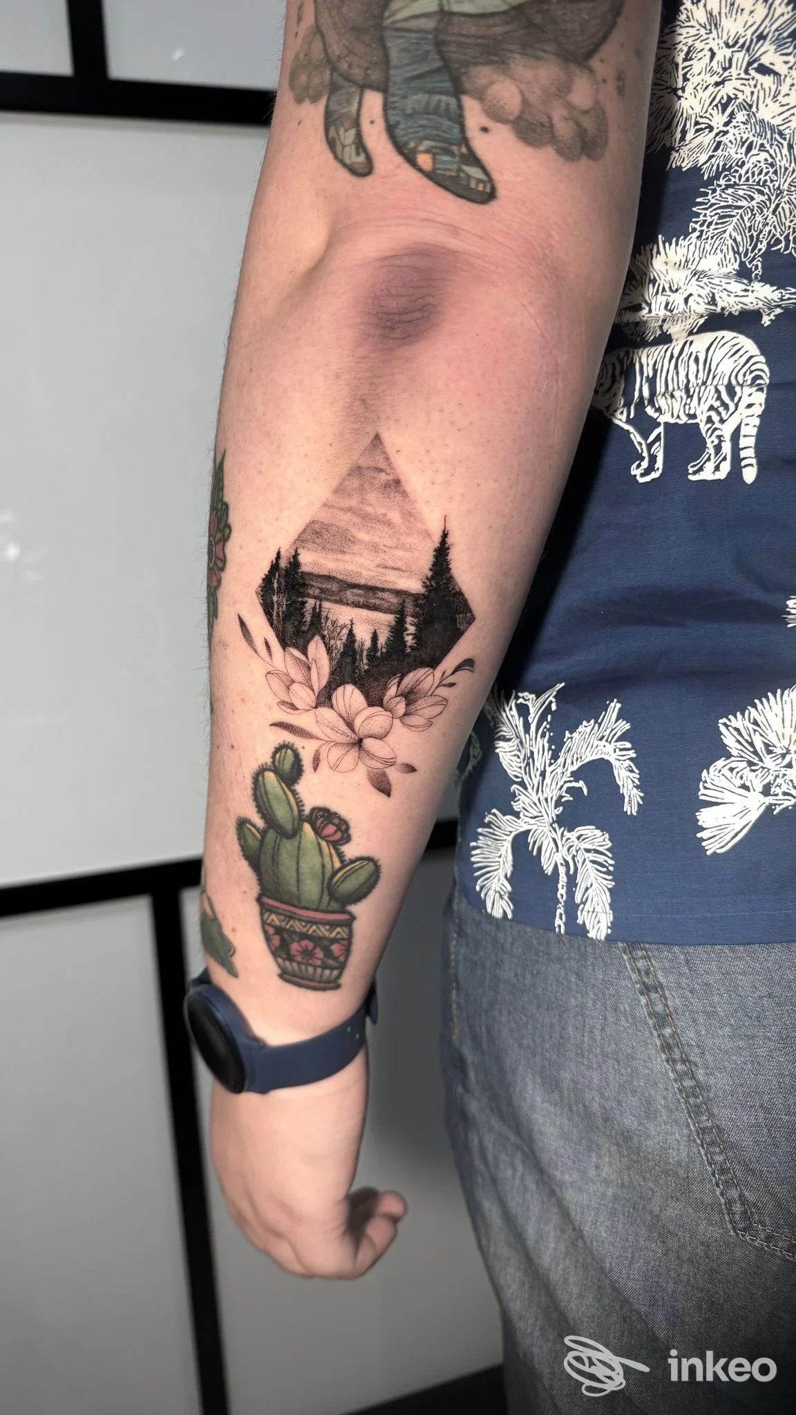 Tatuaggio su avambraccio con paesaggio a forma triangolare, fiori e un cactus; mAmà Tattoo&Co., La Spezia.