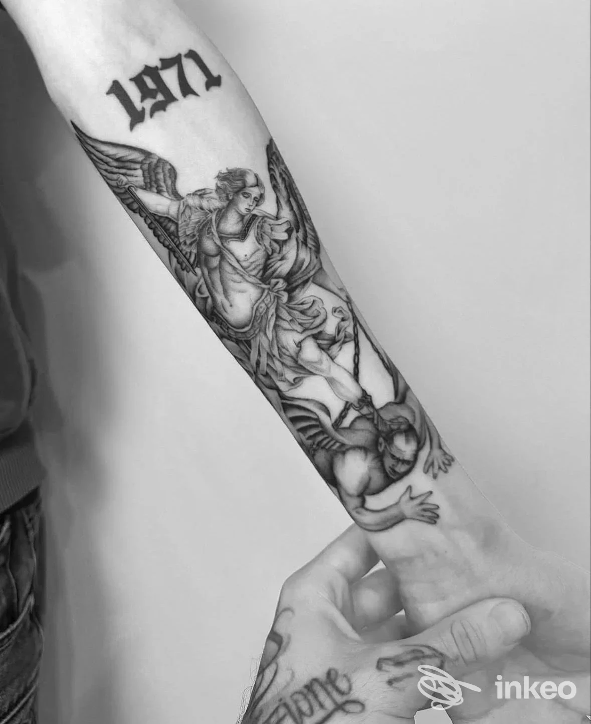 Tattoo presente sull’avambraccio: disegno in bianco e nero di angeli su pelle, nessun volto intero visibile, inquadratura chiara e nitida.