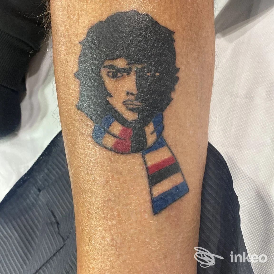 Tatuaggio su avambraccio di una testa stilizzata con sciarpa a righe, immagine fornita da The Cult Tattoo Studio, Genova.
