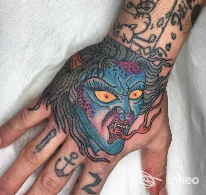 Tatuaggio colorato a testa demoniaca sul dorso della mano, fotografia fornita da Alien8 Tattoo Studio a Savona.