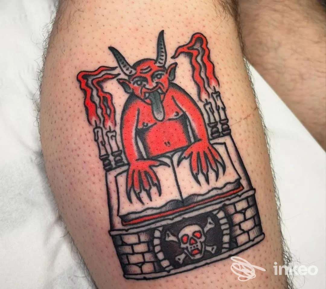 Tattoo a colori su pelle raffigurante un demonio rosso con corna, poggiato su un libro, con cornice di pietra sul braccio/-gamba.