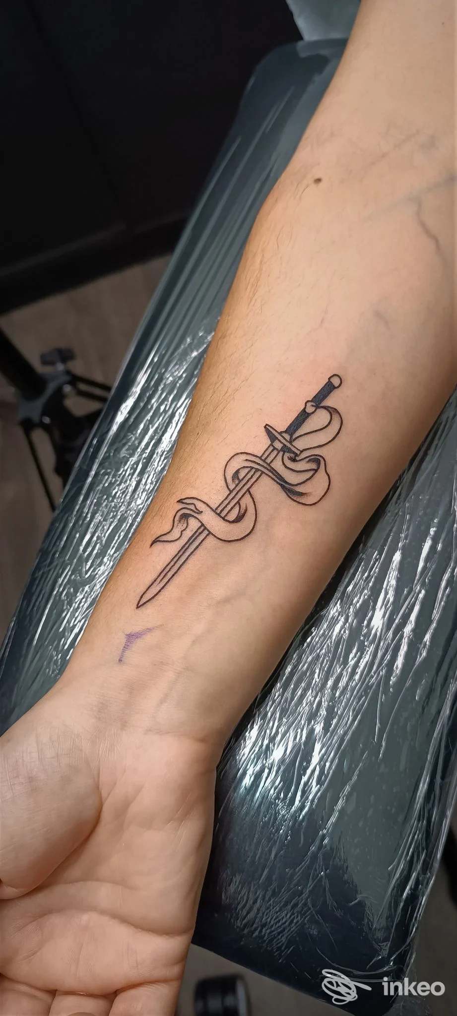 Tattoo realistico su avambraccio raffigurante una spada avvolta in una fascia, posizionata lungo il braccio sinistro.