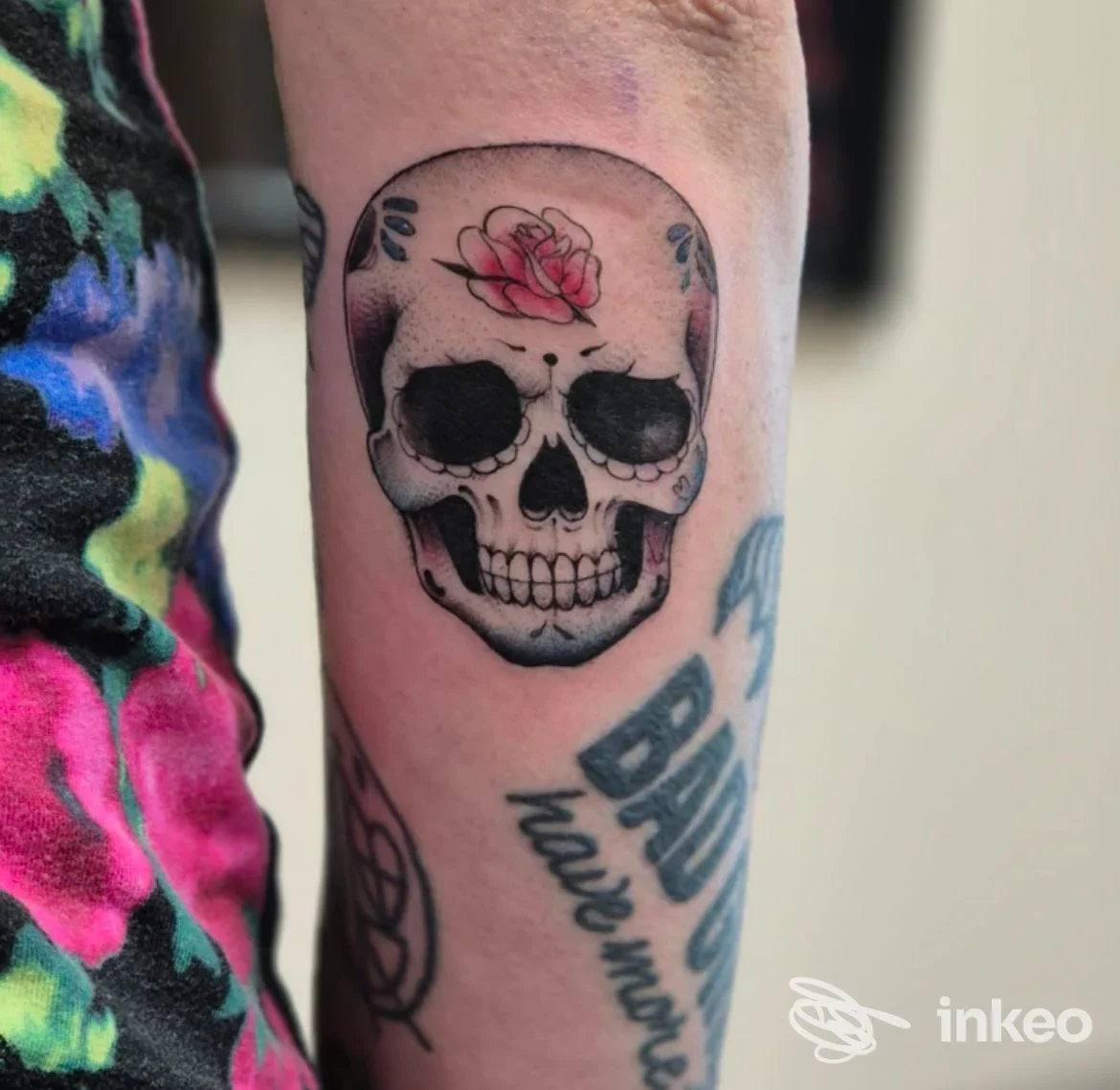 Tatuaggio di un teschio con piccolo fiore rosa sull'avambraccio, realizzato da Ordine sparso Tattoo e Trucco permanente di Federica Obinu a Orbassano.