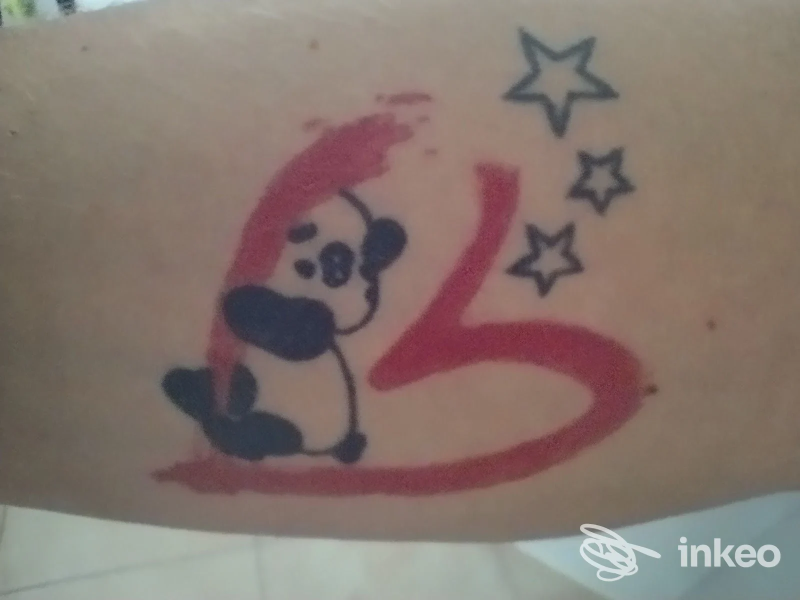 Tatuaggio su avambraccio con panda stilizzato, pennellata rossa a forma di cuore e tre stelline. Ordine sparso Tattoo e Trucco permanente, Orbassano.