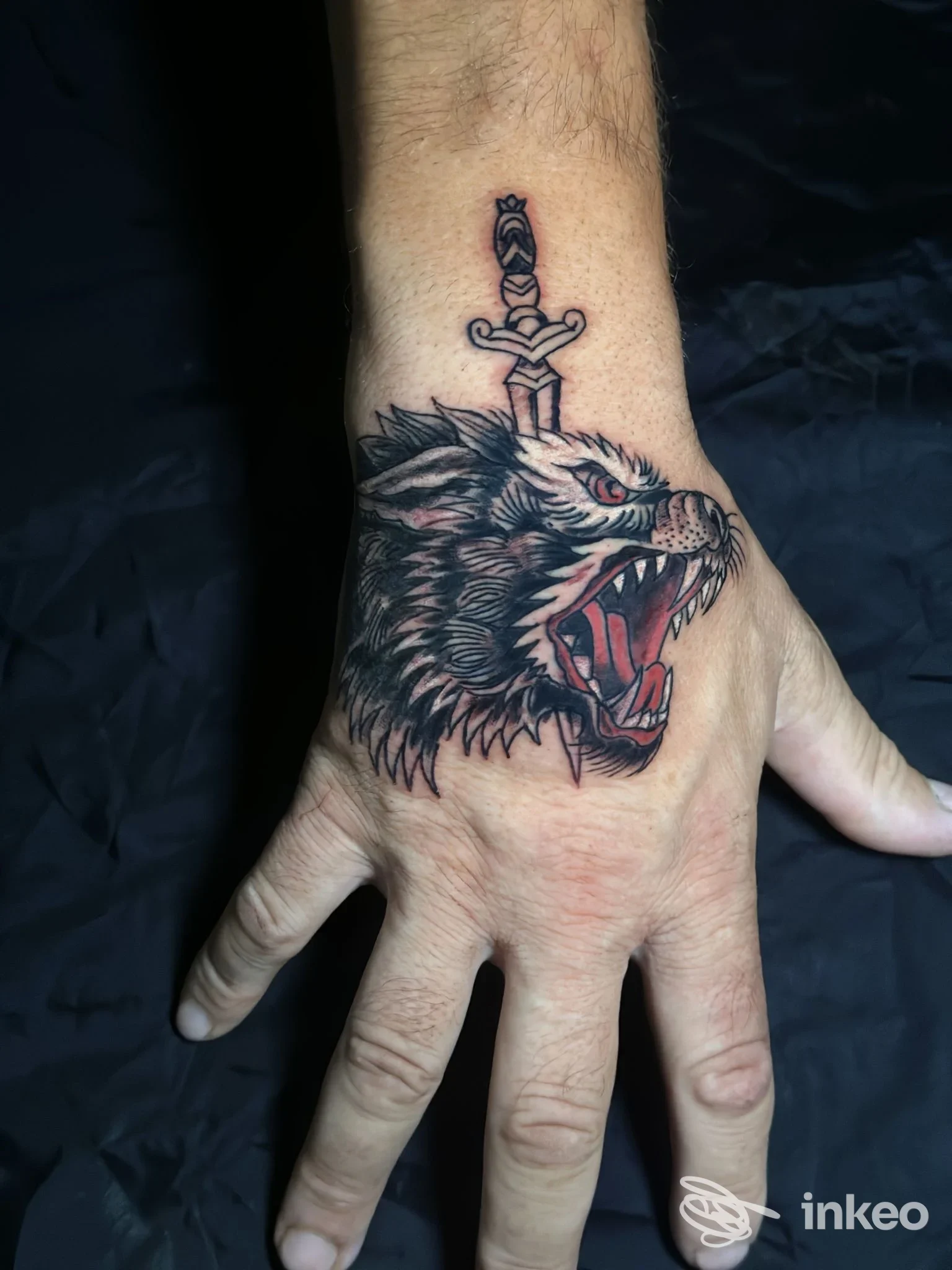 Tatuaggio stilizzato di testa di lupo trafitta da un pugnale sul dorso della mano, realizzato da Trio Tattoo a Torino.