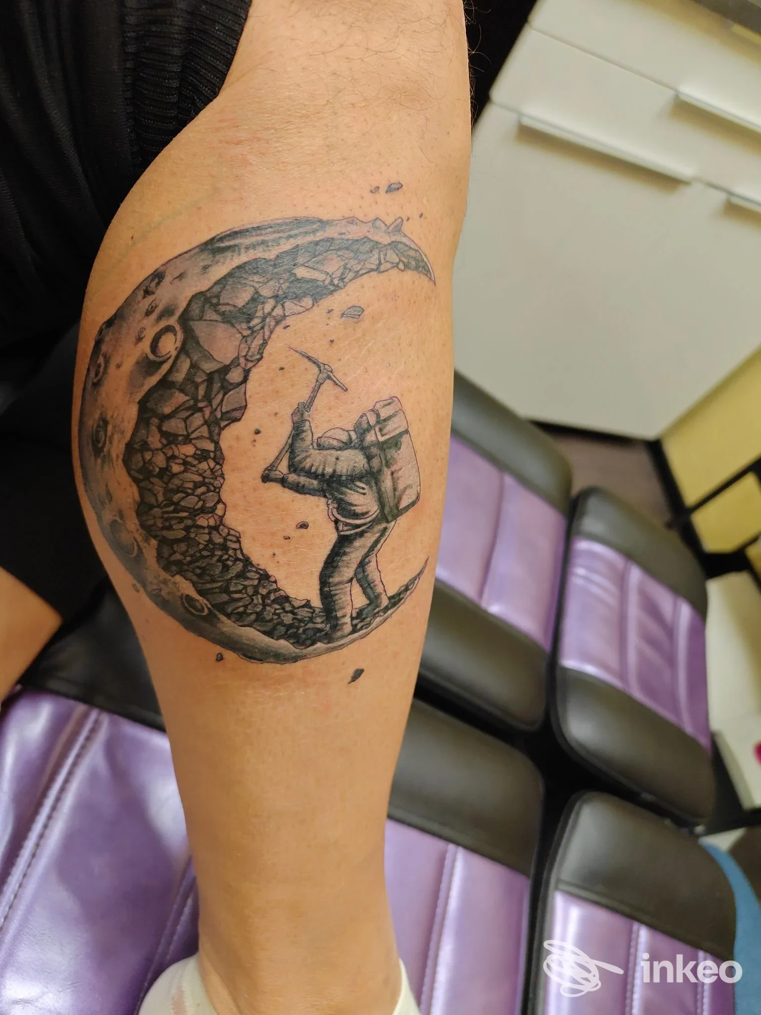Tatuaggio realistico in nero e grigio di una mezzaluna fratturata con un astronauta che scava, sul polpaccio. Trio Tattoo, Torino.