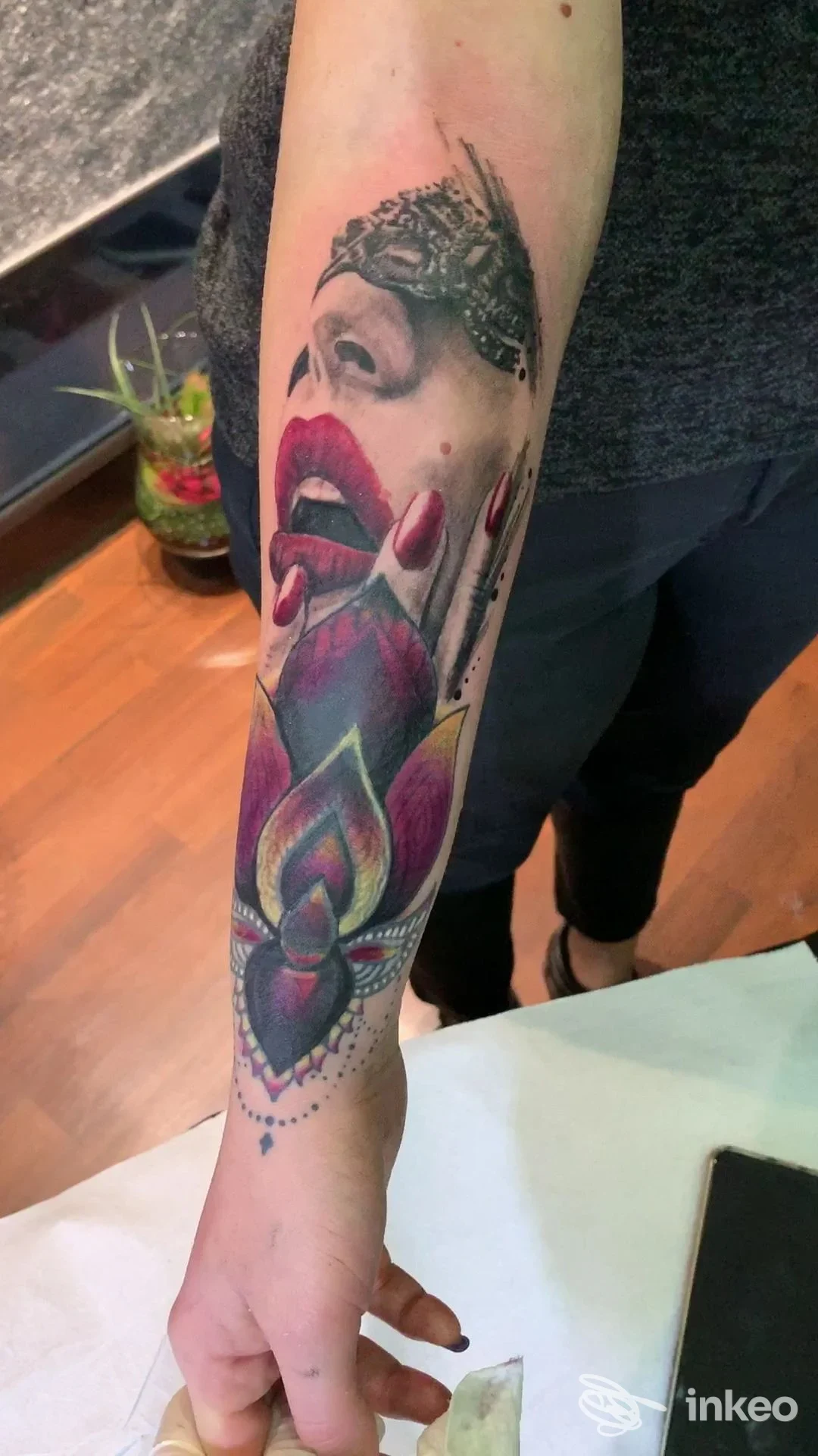 Tatuaggio realistico e colorato su avambraccio fotografato da Venere Ink Tattoo, Torino, con volto parziale e motivi floreali.