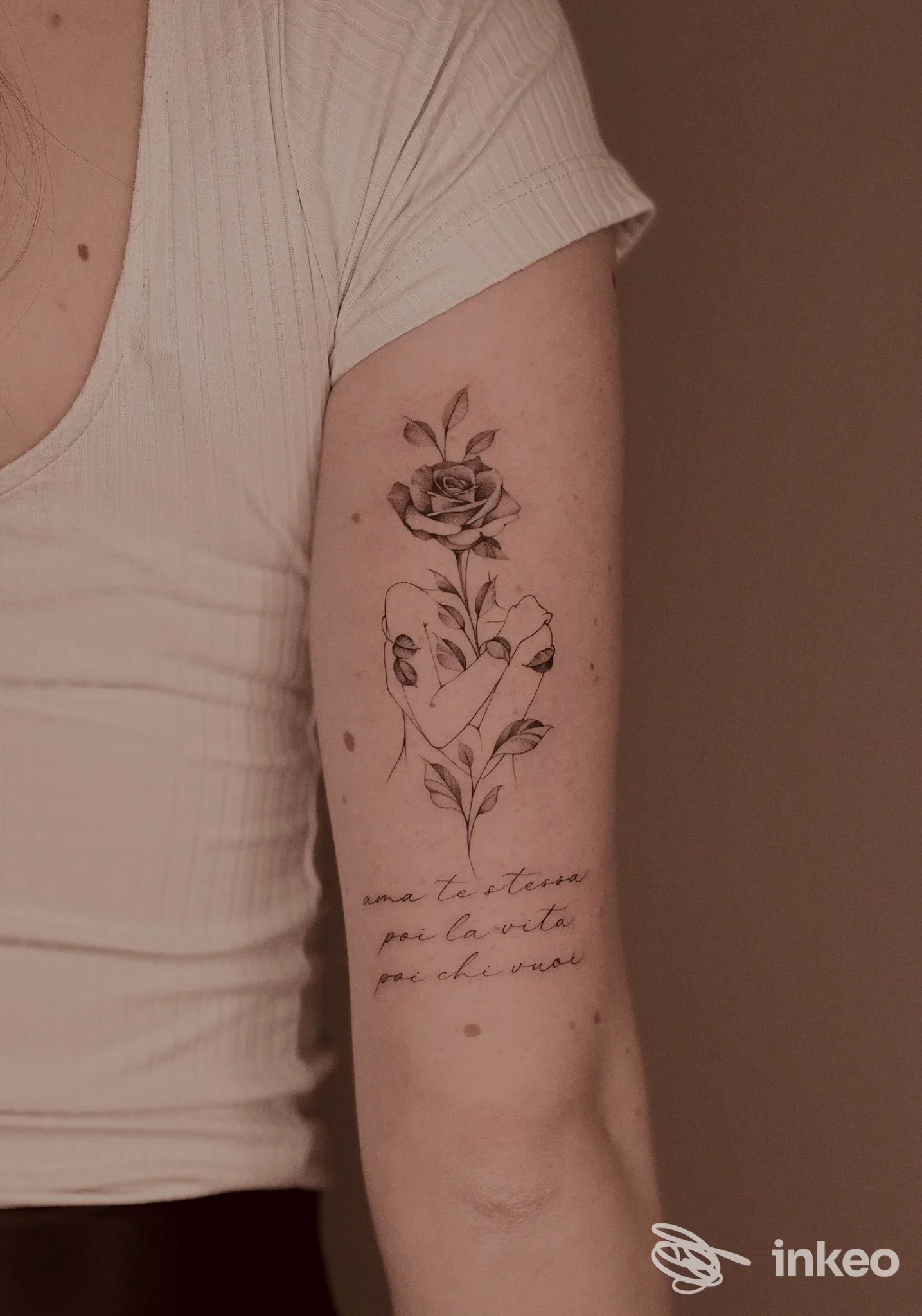 Avambraccio sinistro con tatuaggio a rosa e mano che stringe lo stelo, testo in corsivo sotto la figura, senza volto visibile.