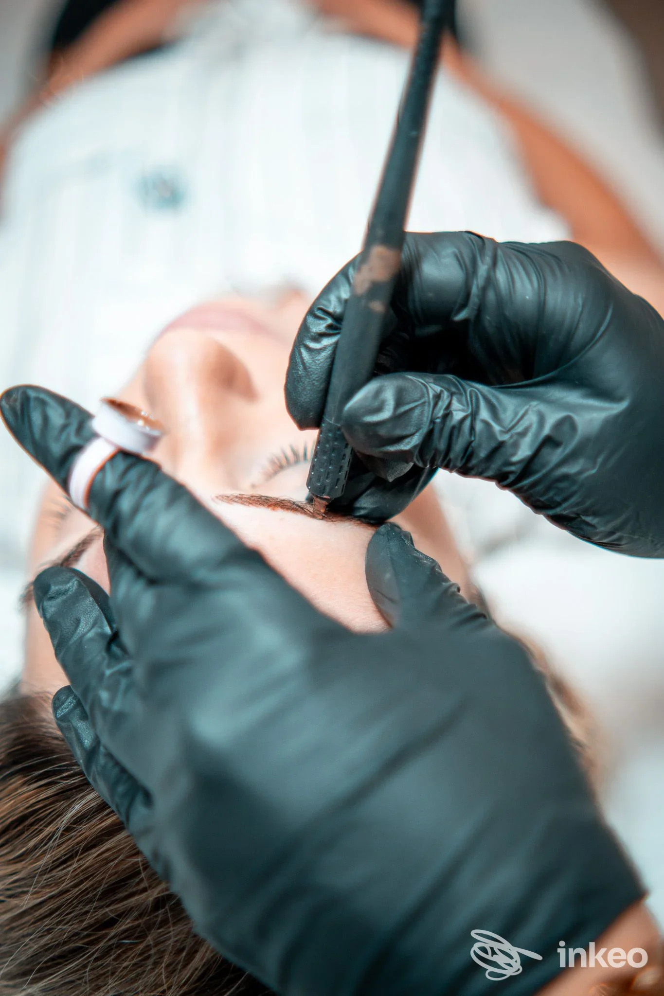 Microblading sopracciglia eseguito su cliente sdraiata, mani con guanti neri in azione nello studio Arianna Pascale, Castellana Grotte.