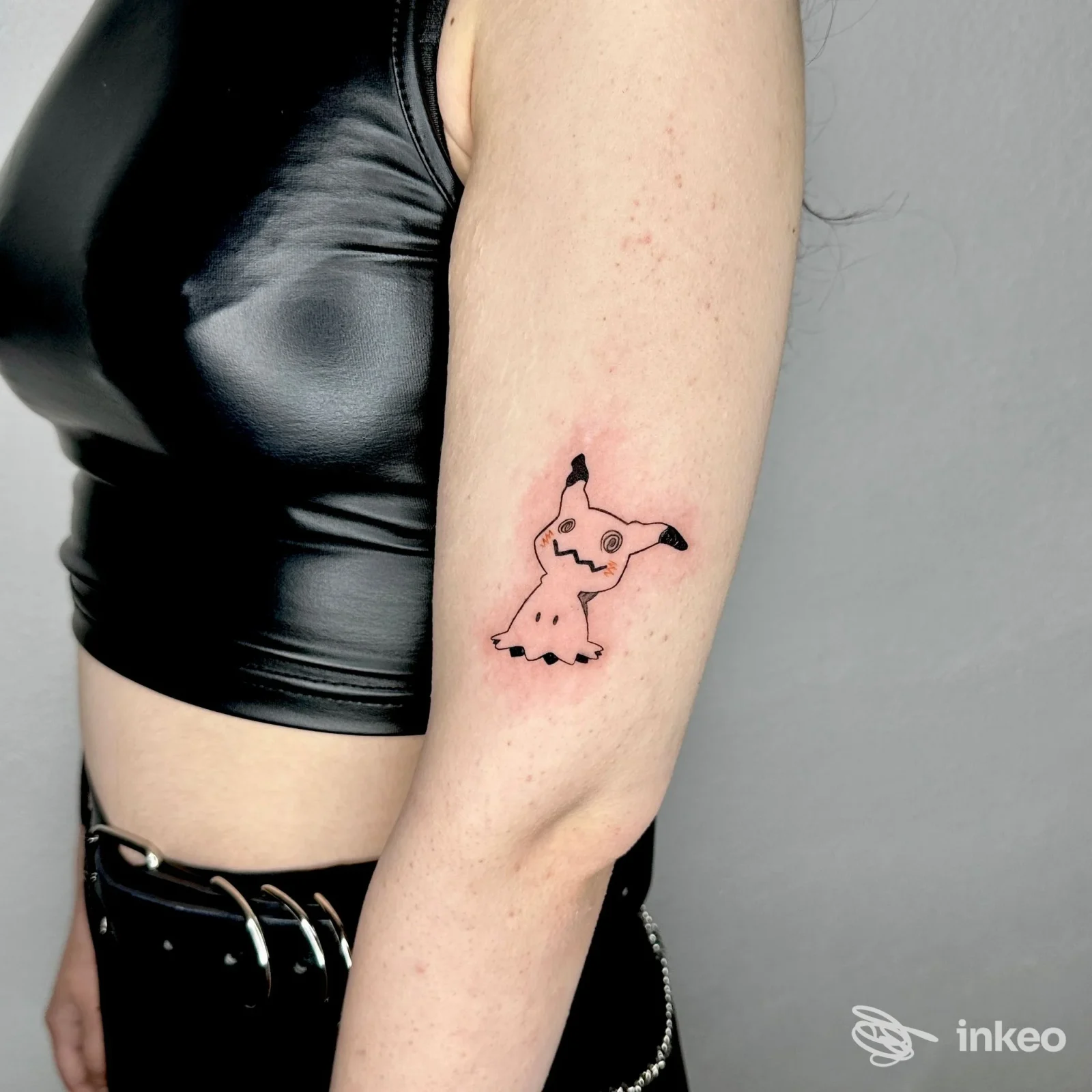 Piccolo tatuaggio a linee nere raffigurante una figura cartoonesca sul braccio esterno, immagine fornita da SharonSka - tattoo • pmu • piercing, Sarule.