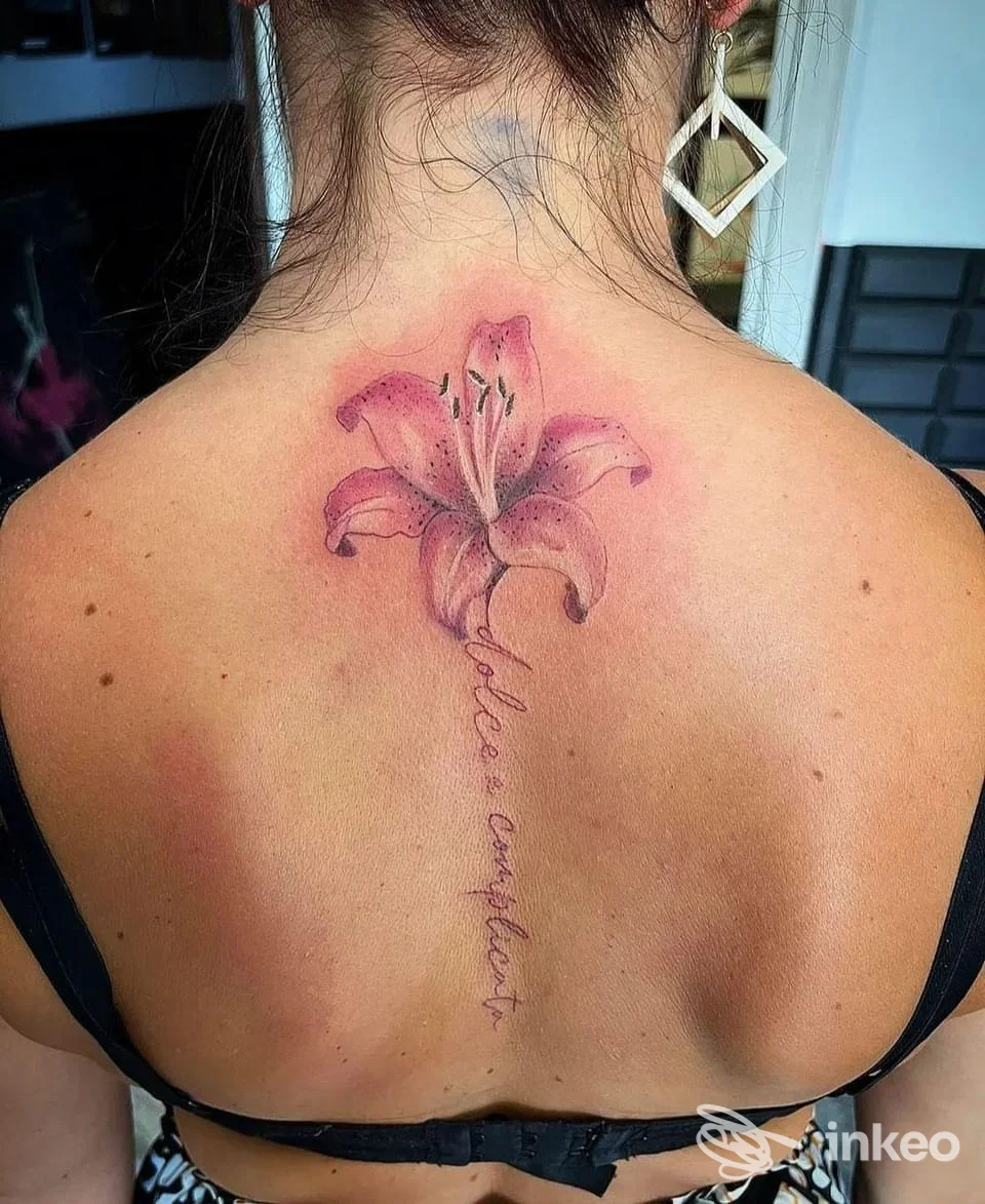 Tattoo di un giglio rosa sulla schiena di una persona, con scritte verticali lungo la colonna.