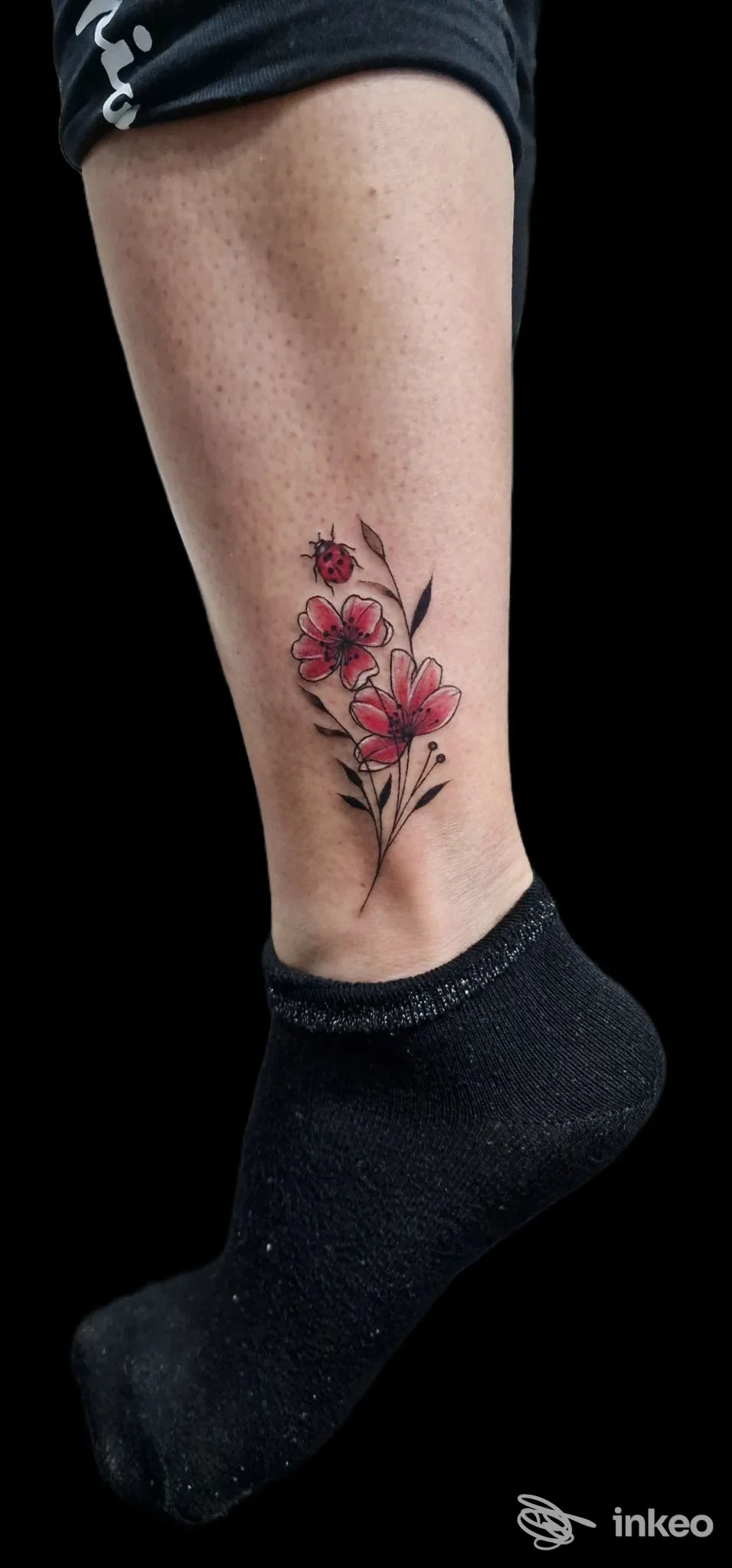 Tatuaggio floreale con coccinella sulla parte inferiore della gamba, realizzato da Clody Tattoo Studio a Capo d'Orlando.