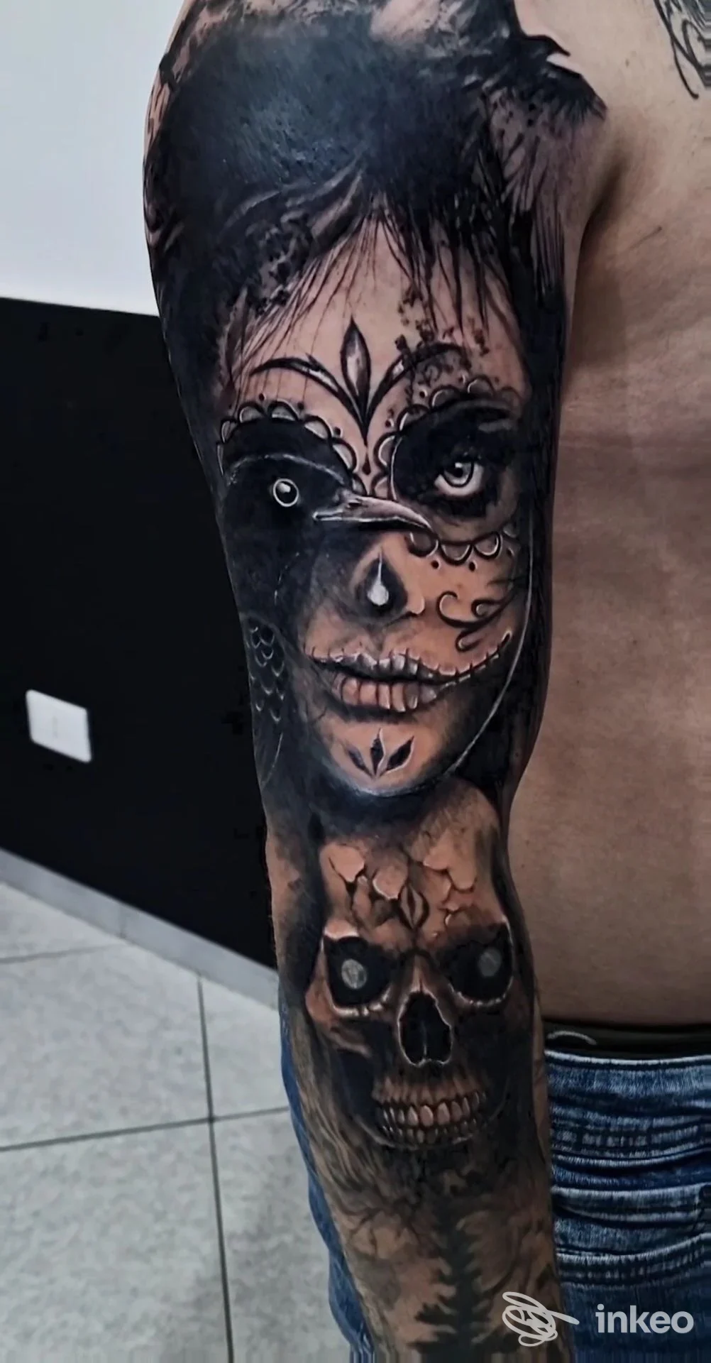 Tatuaggio manica in bianco e nero sul braccio con volti stilizzati e teschio, foto di Clody Tattoo Studio a Capo d'Orlando.