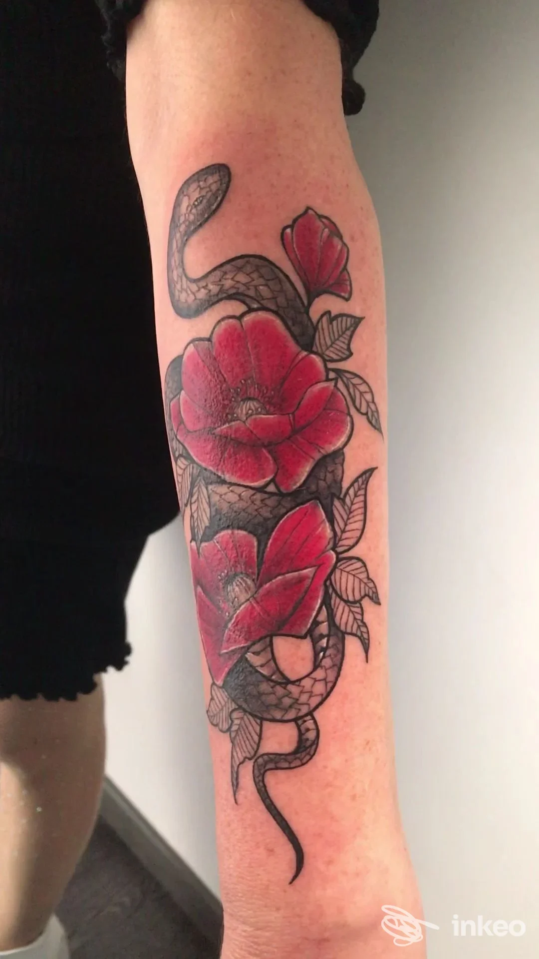 Tatuaggio su avambraccio con serpente avvolto e fiori rossi, realizzato da INK TATTOOs a Capo d'Orlando.