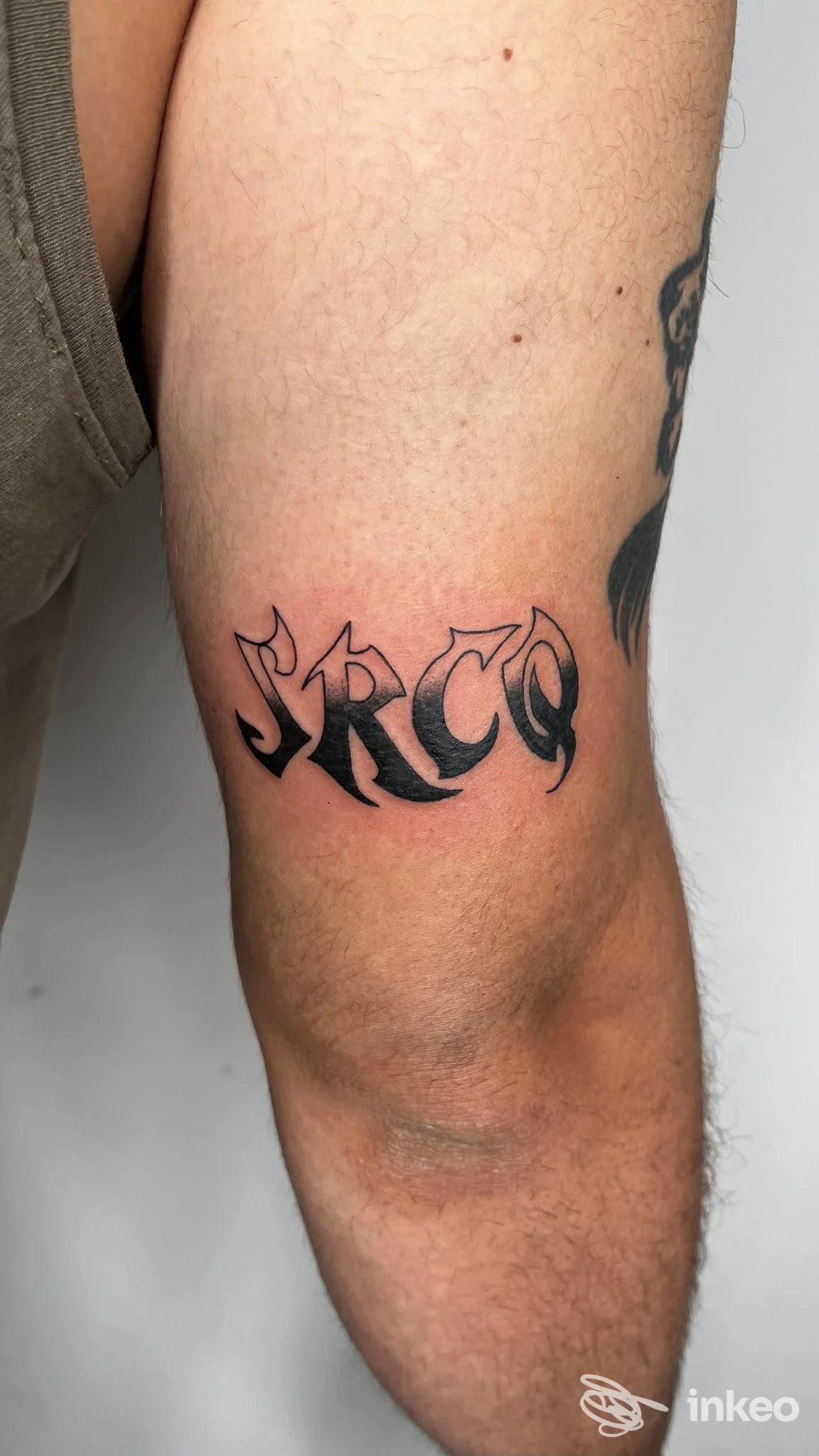 Tattoo in stile lettering gotico sul braccio, tatuaggio nero visibile su pelle reale, senza overlay né volto visibile, foto focalizzata sul braccio.