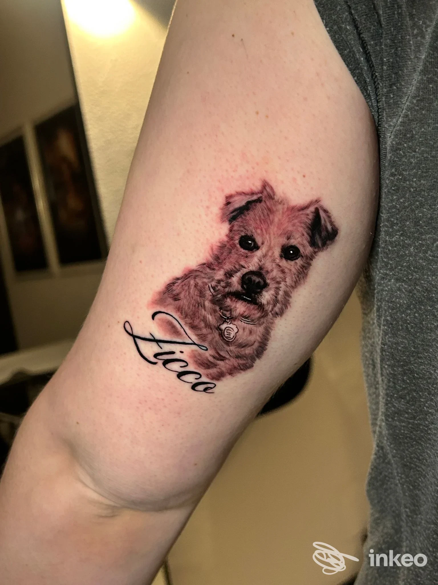 Tatuaggio realistico di un piccolo cane con nome Luca sull’avambraccio sinistro, effetto pelle visibile e dettagli scuri.