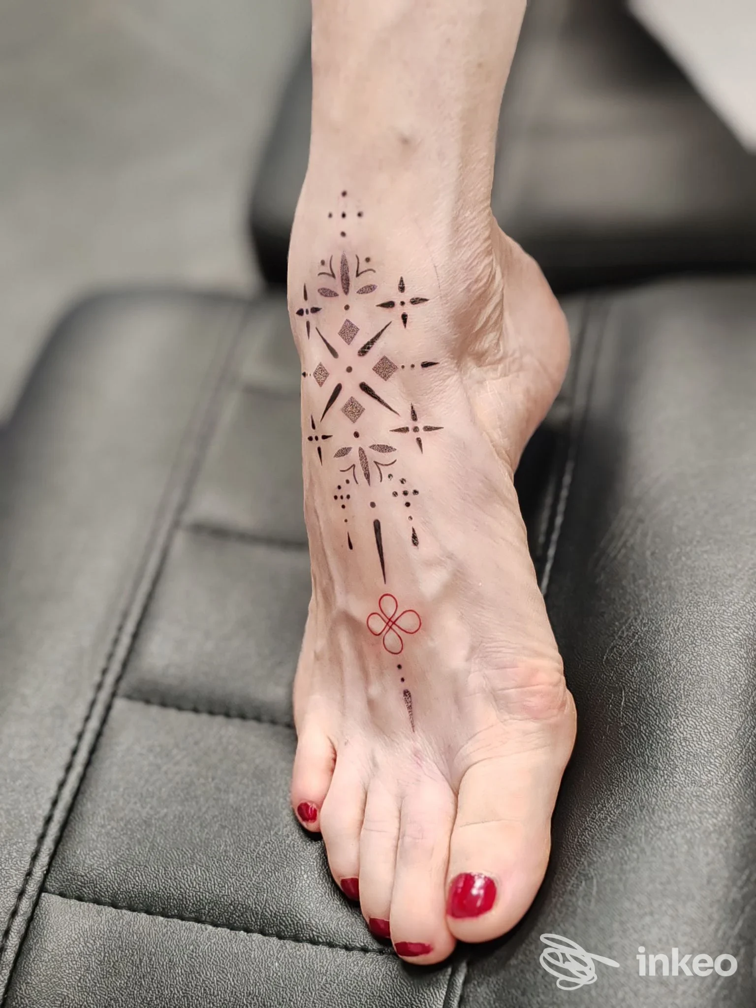 Tatuaggio geometrico e puntinato sul dorso del piede, con piccolo elemento rosso; foto per Iside Tattoo Studio, Mirano.
