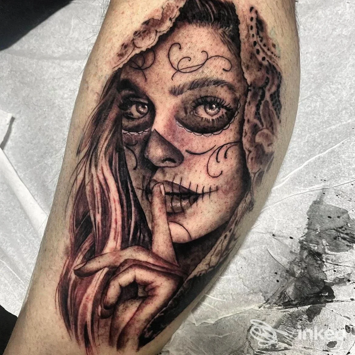 Tatuaggio realistico sugar skull con volto femminile e dito sulle labbra, su avambraccio.
