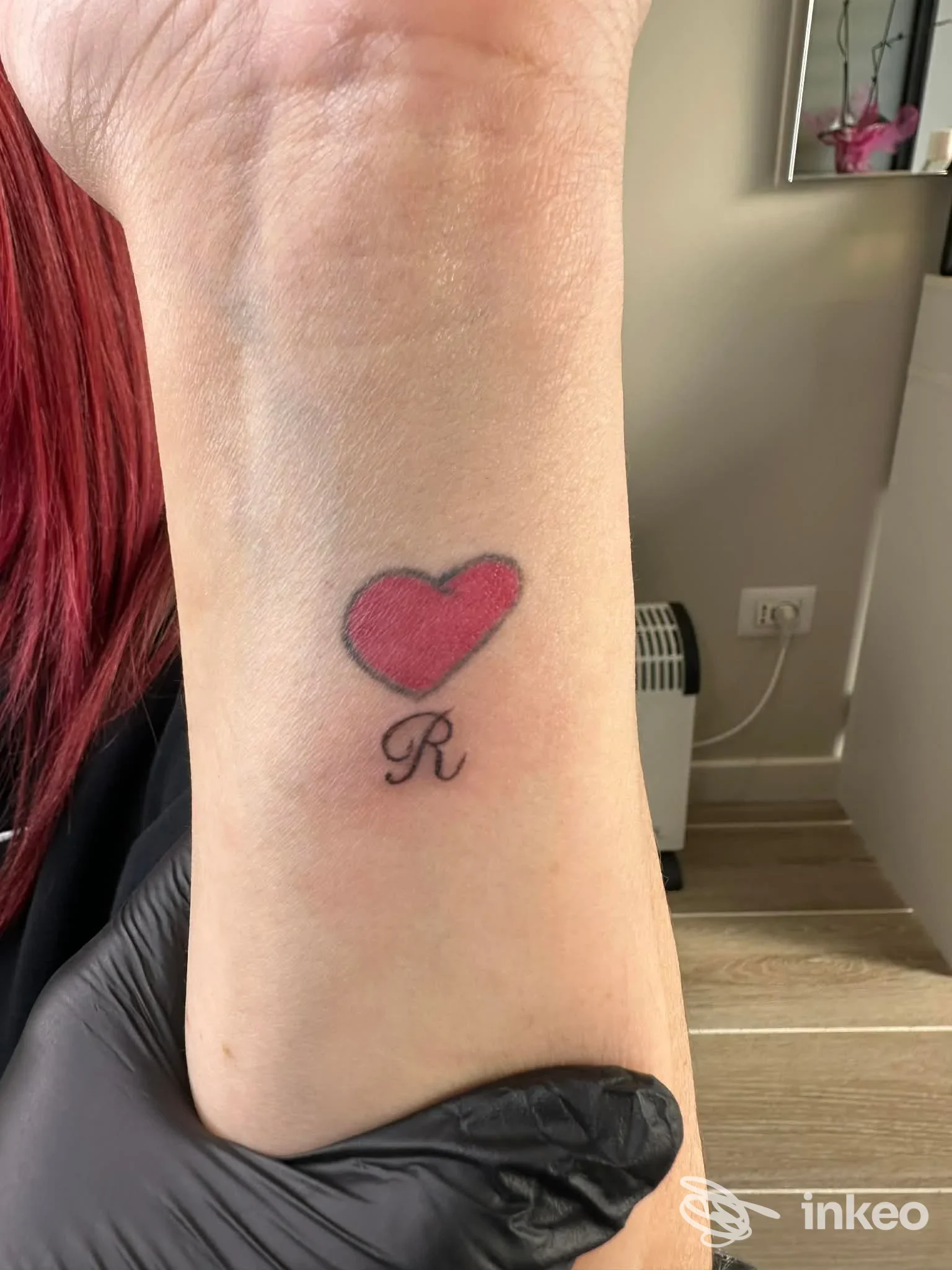 Tatuaggio semplice di un cuore rosso con la lettera 'R' sul polso interno, realizzato da Naty Strun, Studio Tattoo & Permanent Make-up, Venezia.