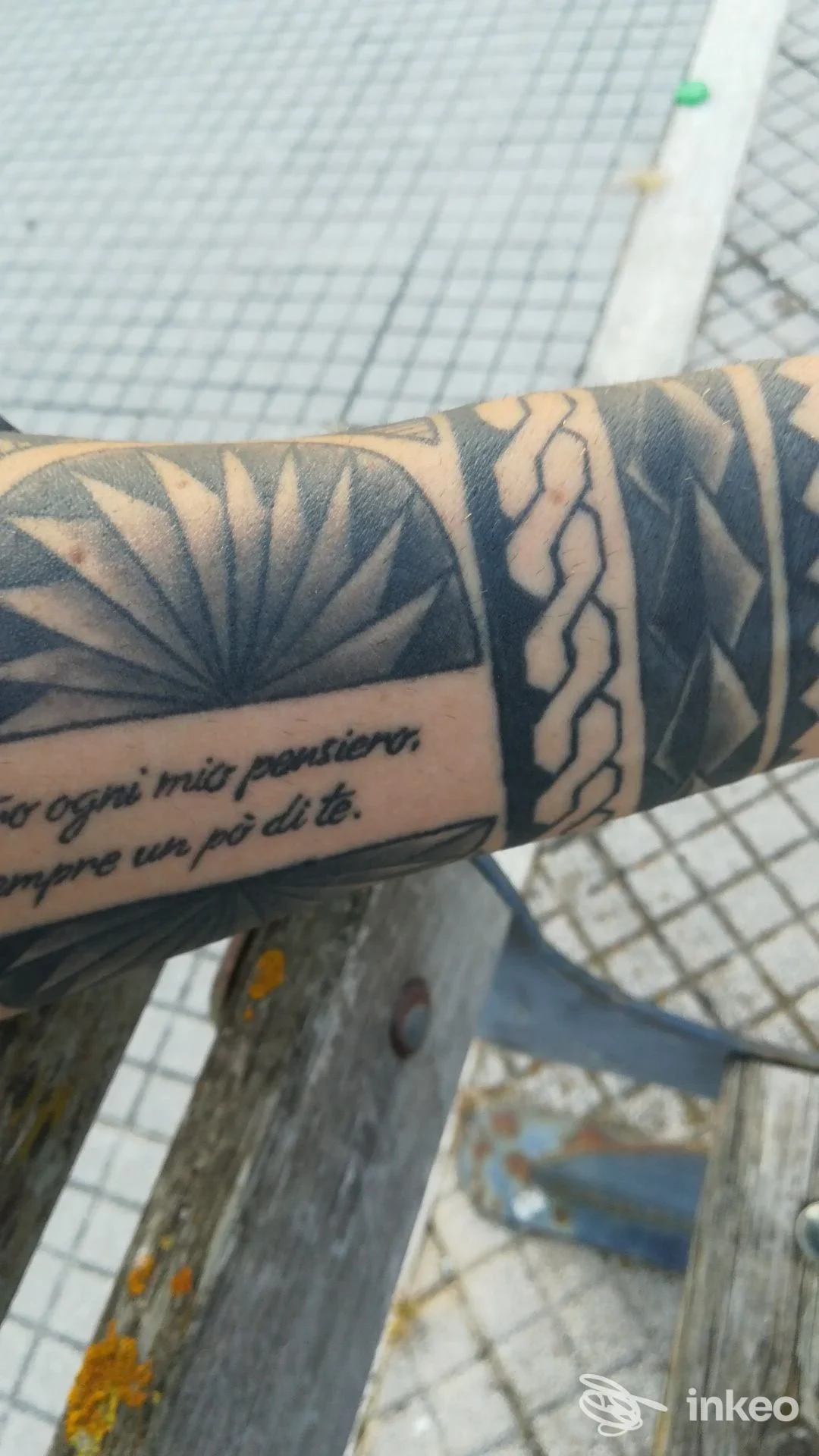 Primo piano di un avambraccio tatuato con motivi geometrici e testo, foto fornita da Àkros Tattoo Studio, Recanati.