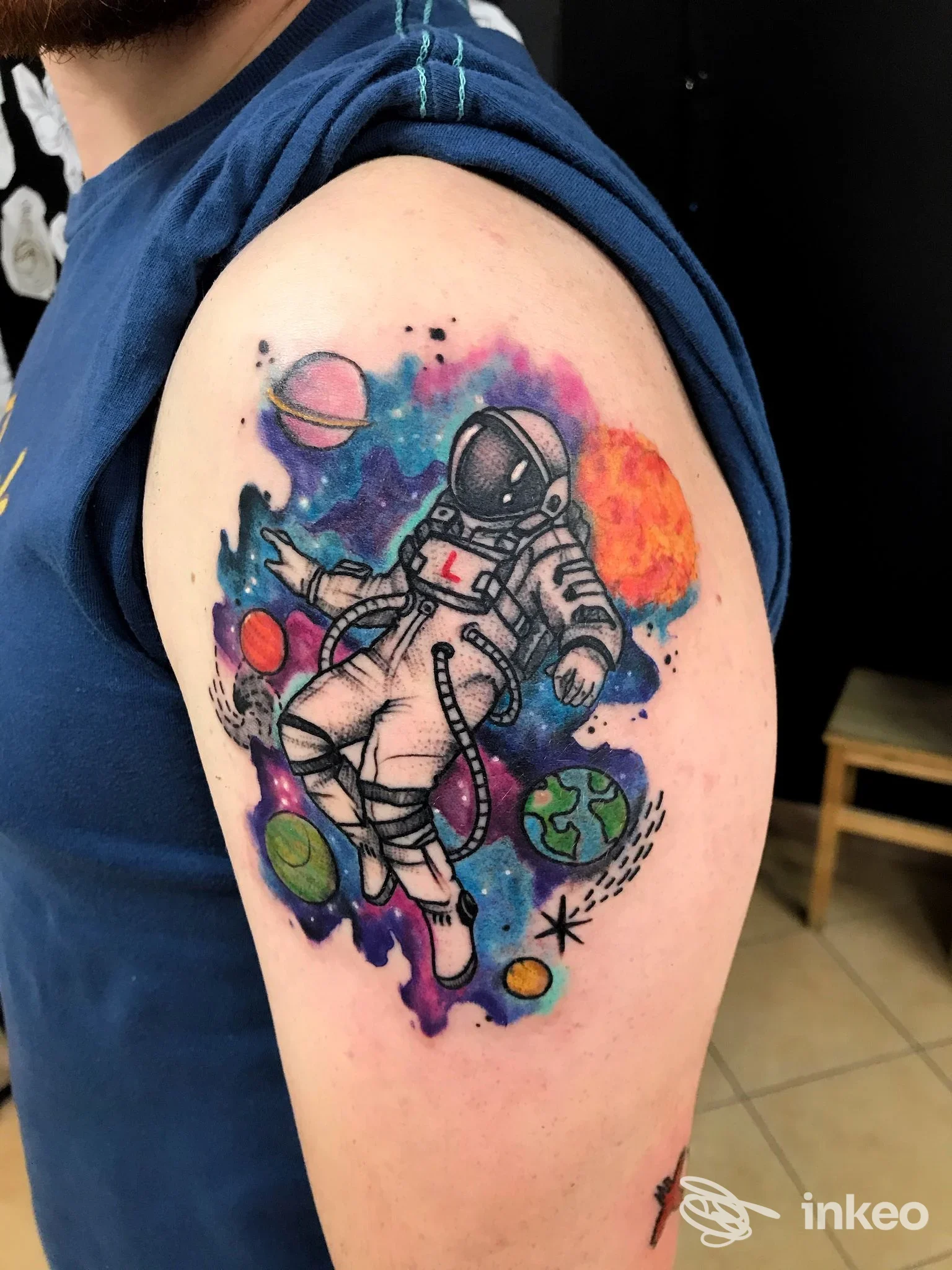 Tatuaggio colorato di un astronauta con pianeti sulla parte superiore del braccio, realizzato da Alchemy Tattoo Studio a Porto Recanati.