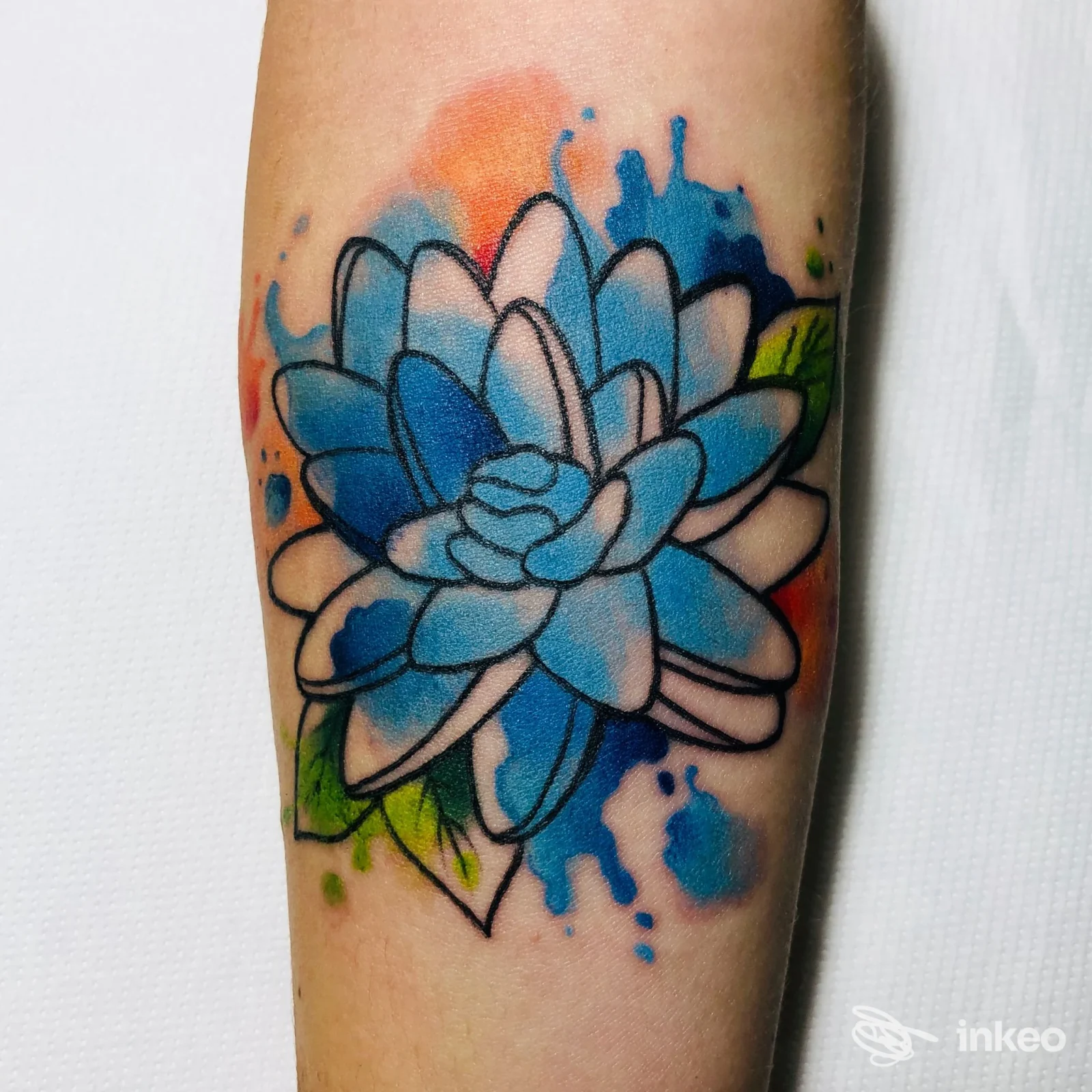 Tatuaggio floreale colorato in blu, bianco e arancione sull'avambraccio, con contorni neri e sfumature tipo acquerello, foto di BarbieSlayer Tattoo a Macerata.