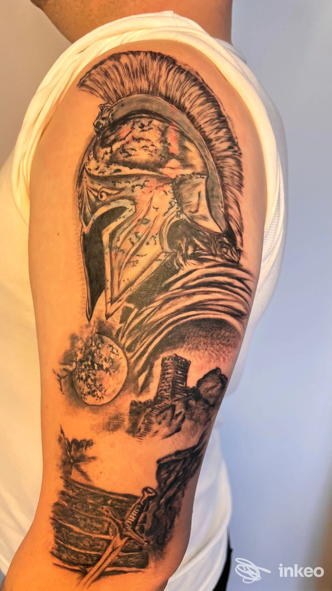 Grande tatuaggio in bianco e nero di un elmo spartano sul braccio superiore, realizzato da Be Unique Tattoo a Marotta.