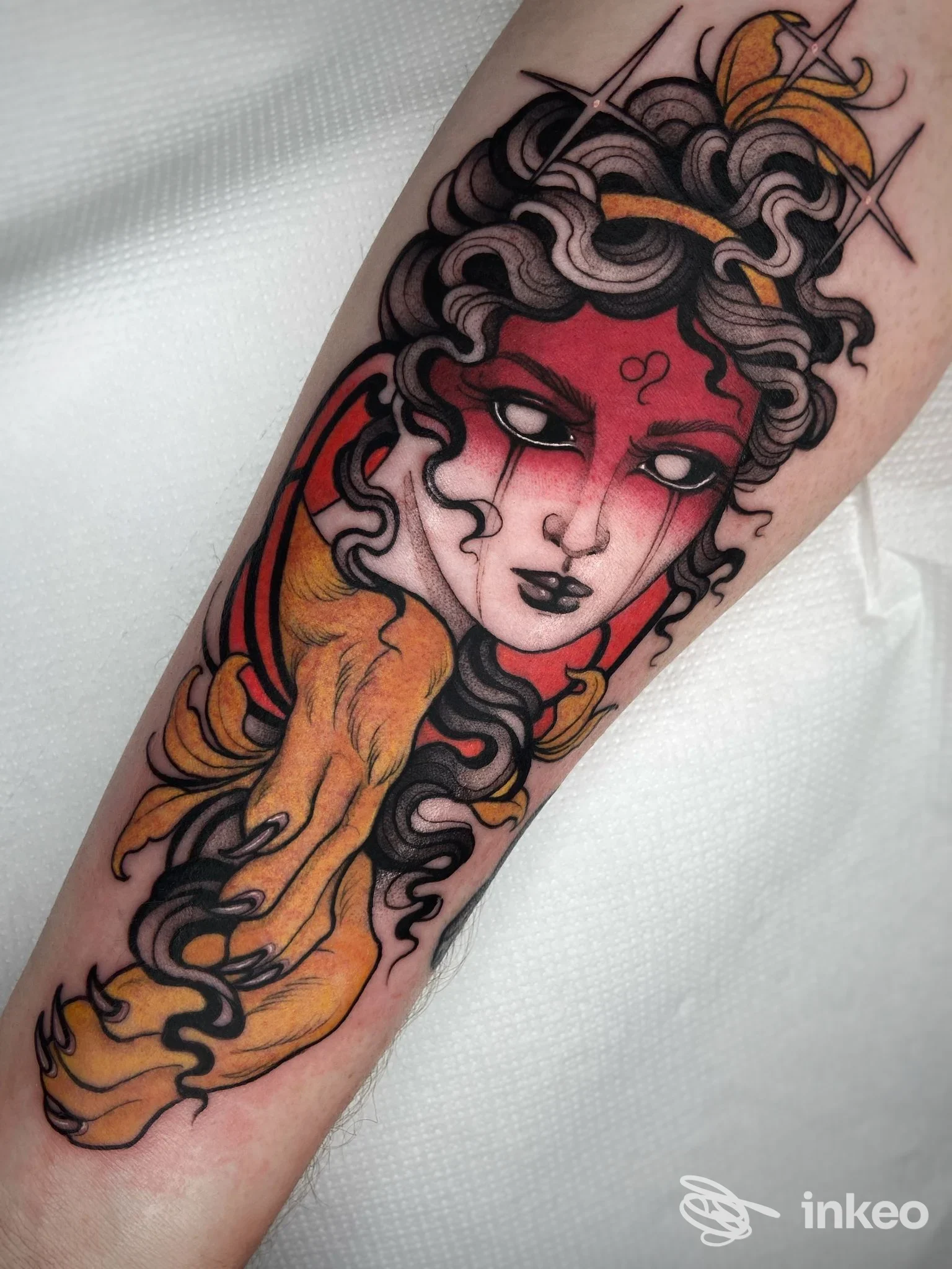 Tatuaggio su avambraccio che raffigura un volto stilizzato con aree rosse, capelli scuri e dettagli gialli — Blue Bamboo Tattoo Studio, Fabriano.