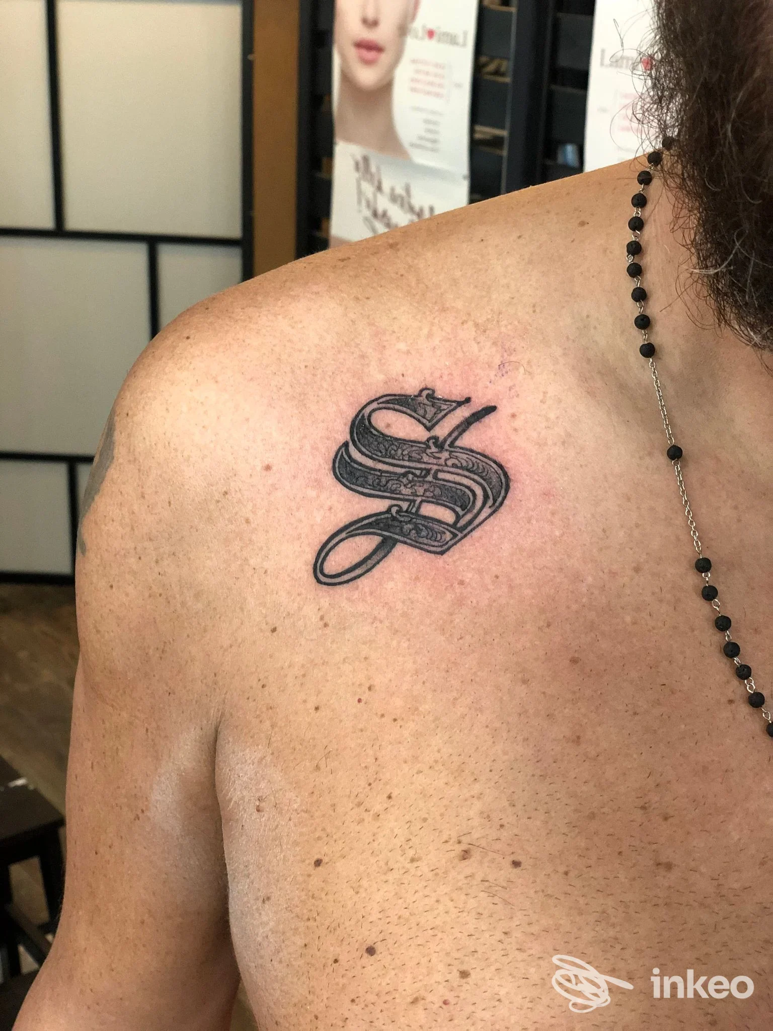Tatuaggio monogramma nero sopra la clavicola sinistra, foto scattata nello studio ARTE SUAVE TATTOO SHOP a Pesaro.