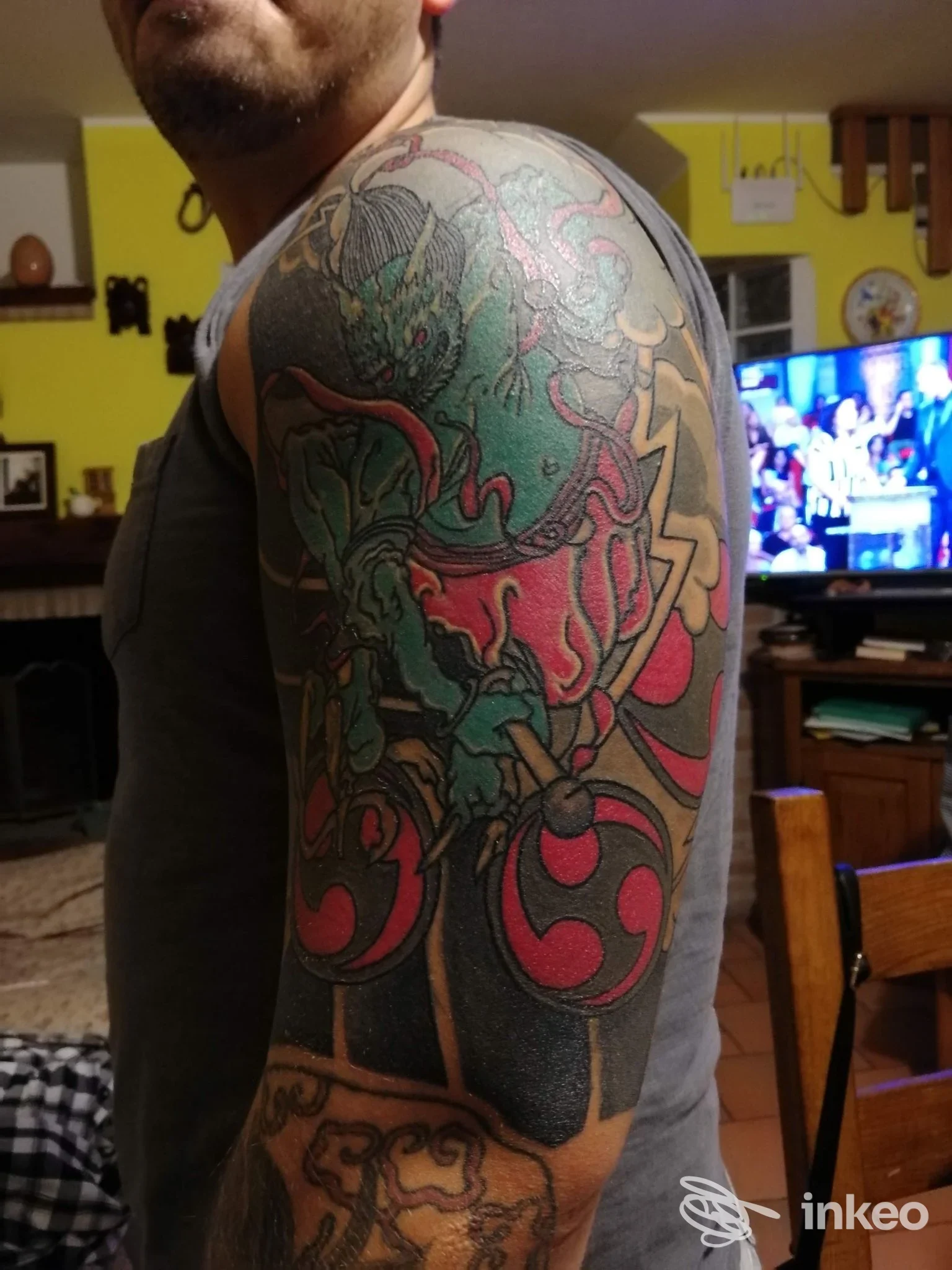Tatuaggio a manica su spalla e braccio superiore eseguito da CQuadro Tattoo Fano, colori verdi e rossi su sfondo scuro, ritratto parziale del soggetto.