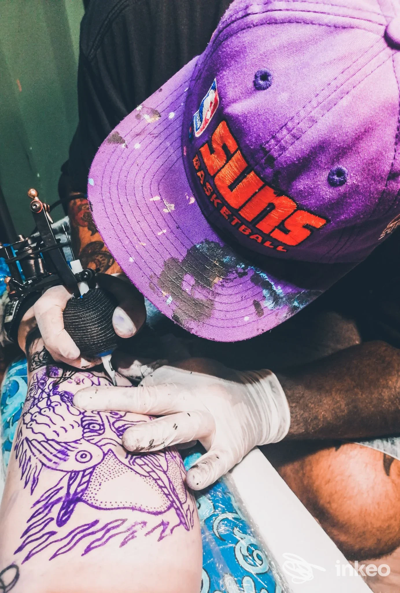 Artista con macchinetta mentre tatua un disegno lineare sul polpaccio. Cry Baby Tattoo Shop, Porto Potenza Picena.