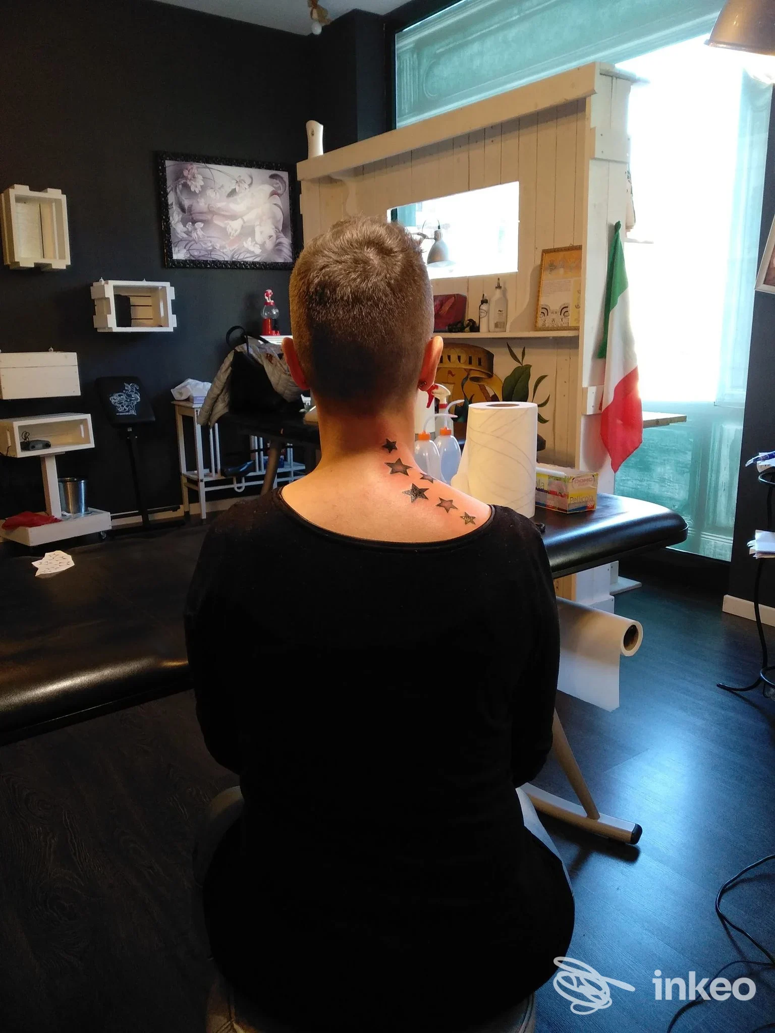 Vista posteriore di una persona seduta nello studio Dayaks Tattoo a Pesaro con un tatuaggio di stelle sul collo/parte alta della schiena.