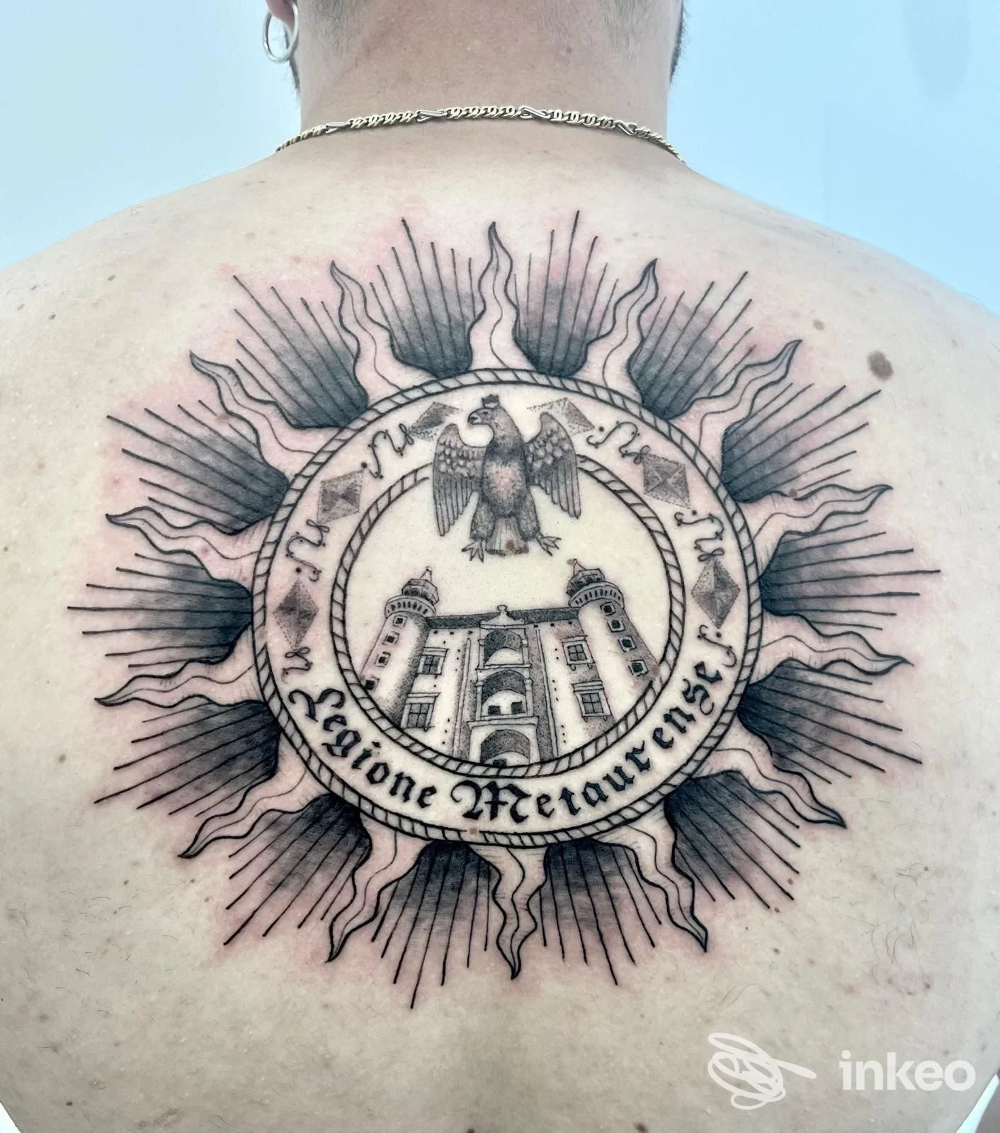 Ampio tatuaggio circolare sulla schiena con edificio e aquila al centro, fotografato nello studio Deeper Think Tattoo a Urbino.