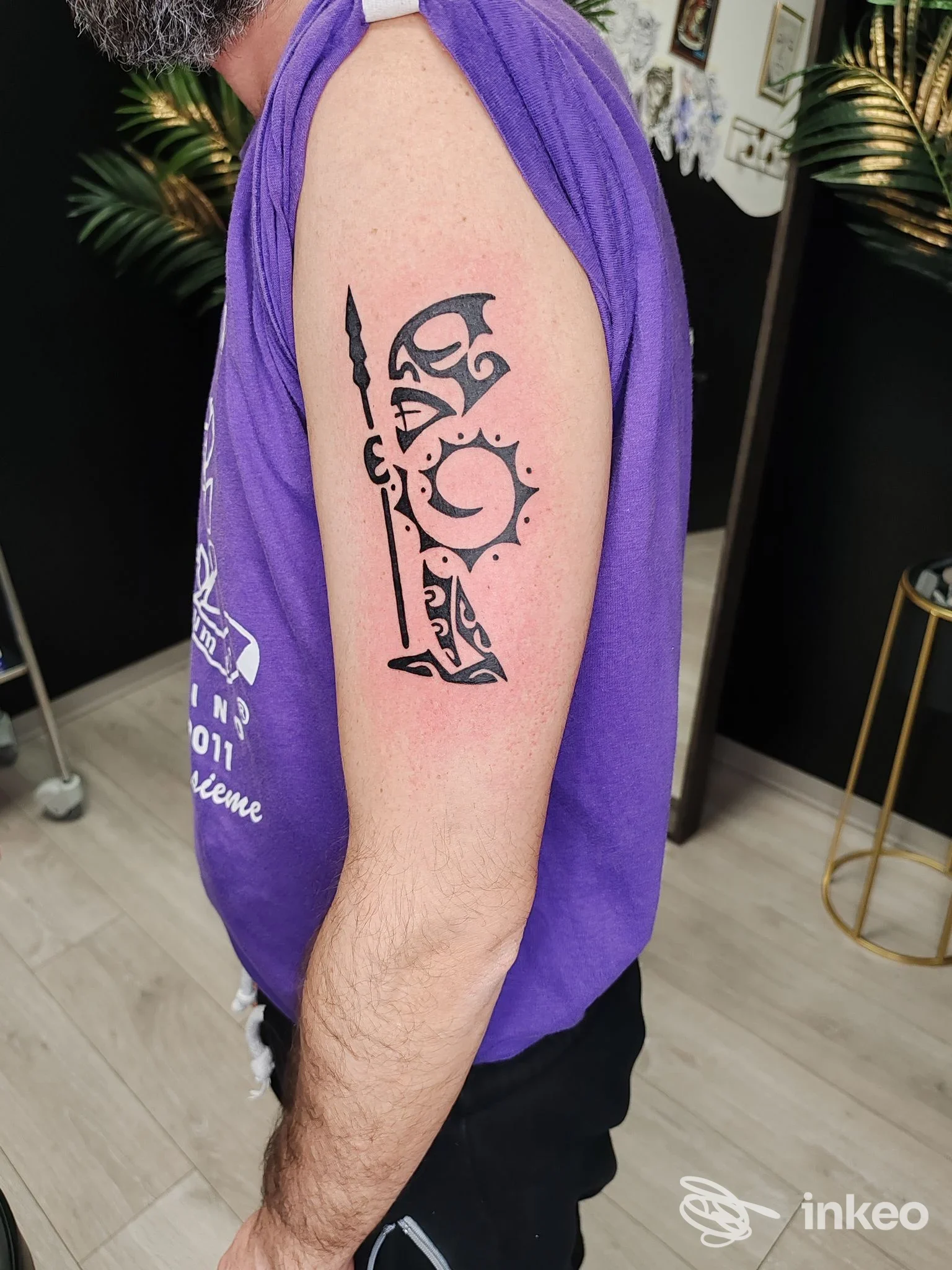 Tatuaggio nero stilizzato sul braccio superiore eseguito presso Diletta Tattoo Vision a Tolentino, foto in studio con soggetto in maglietta viola.