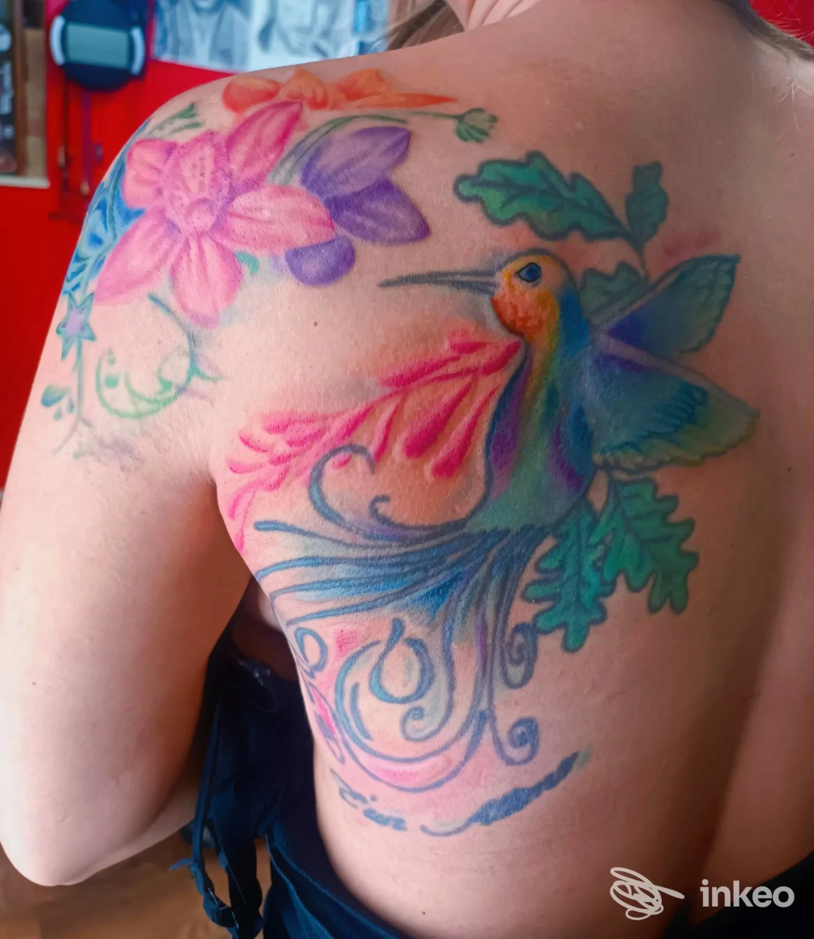 Tatuaggio colorato di un colibrì con fiori sulla schiena e spalla sinistra, lavoro di Dok Tattoo a Villa San Giuseppe.