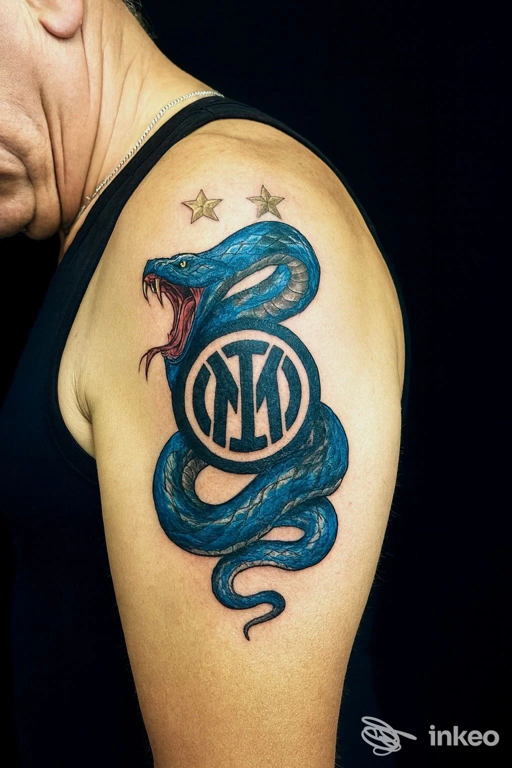 Tatuaggio sulla spalla con serpente blu avvolto attorno a un monogramma e due stelle, fotografato al braccio. Fabio Tattoo Studio, Civitanova Marche.