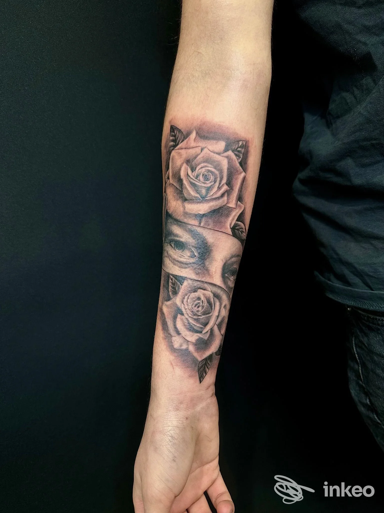 Tatuaggio realistico in bianco e nero su avambraccio con due rose e una porzione di volto, foto fornita da Fabio Tattoo Studio, Civitanova Marche.