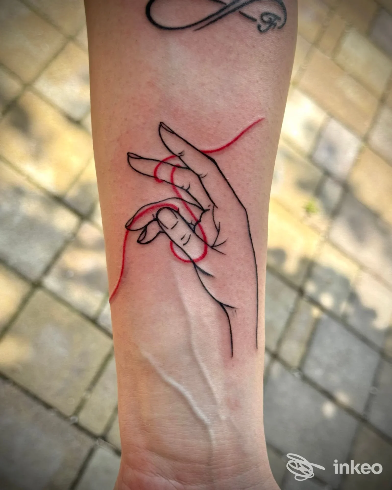 Tatuaggio minimal su avambraccio di mano stilizzata con filo rosso, Gloria Tattoo, Camerino.