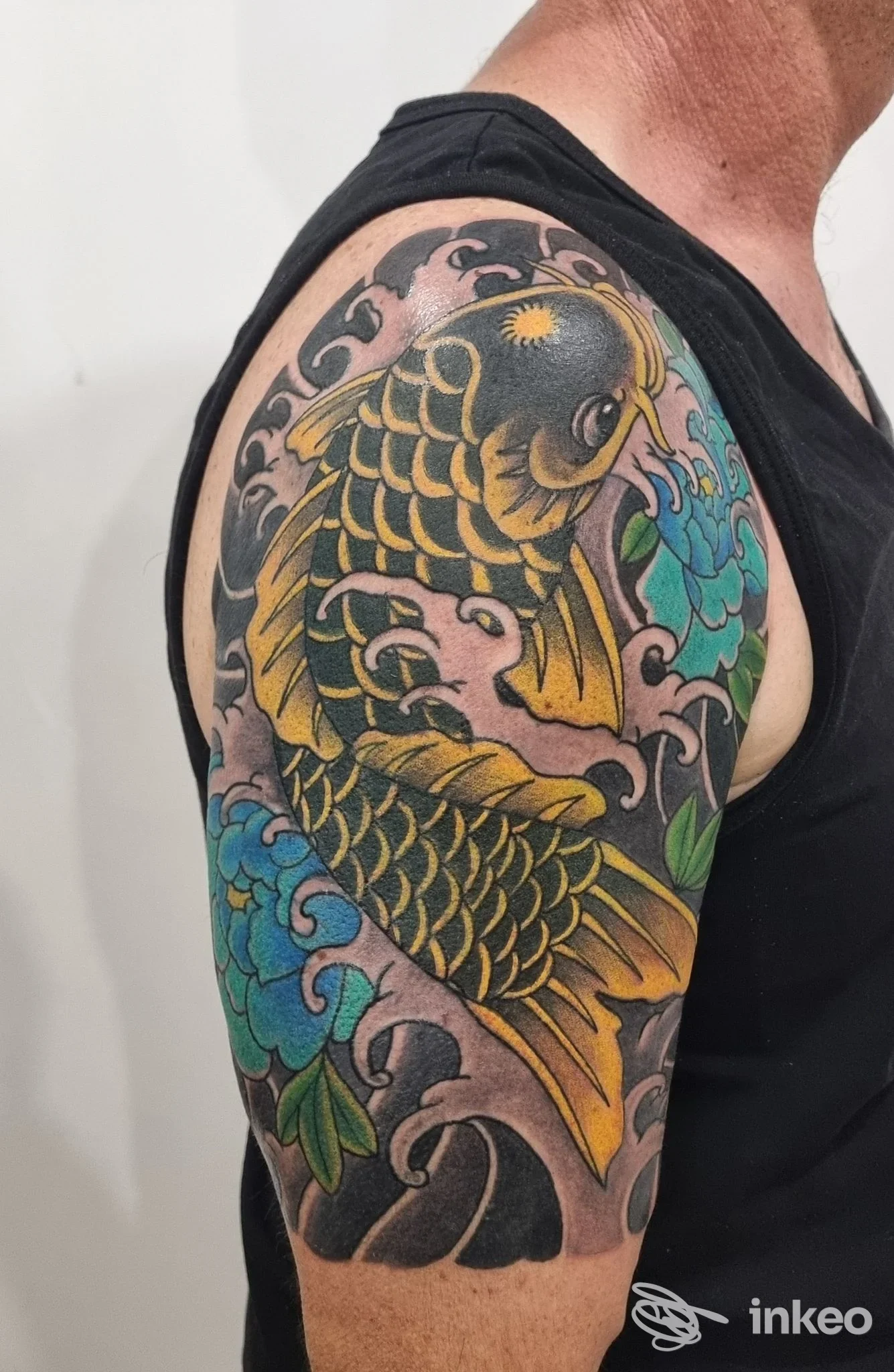 Tatuaggio a tema carpa colorata sul braccio e spalla, Jona Tatuaggi Lauretani, Loreto.
