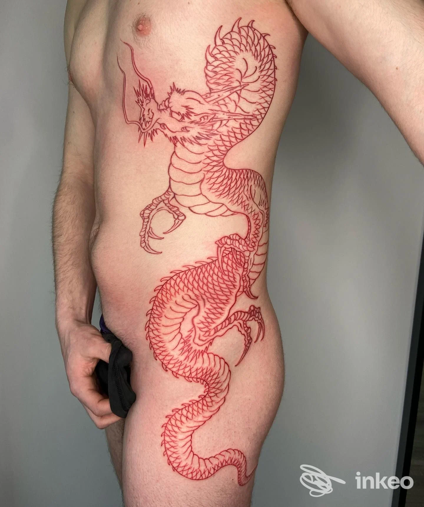Tatuaggio a inchiostro rosso a forma di drago sul fianco e torace, scatto fornito da Magical Ink Tattoo a Fabriano.