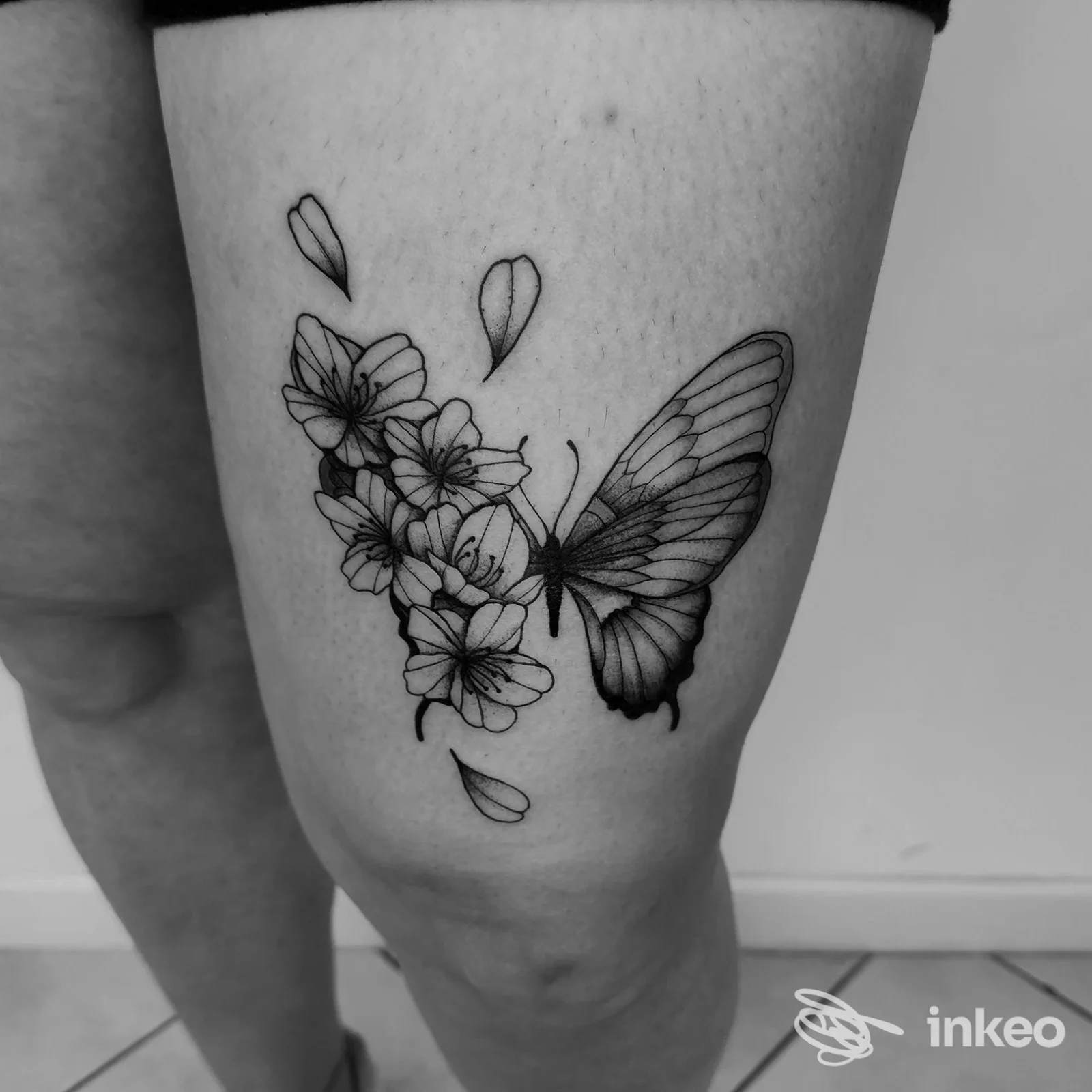 Tatuaggio nero di farfalla e fiori sulla coscia, foto inviata da Malasorte Tattoo Studio a Porto Sant'Elpidio.