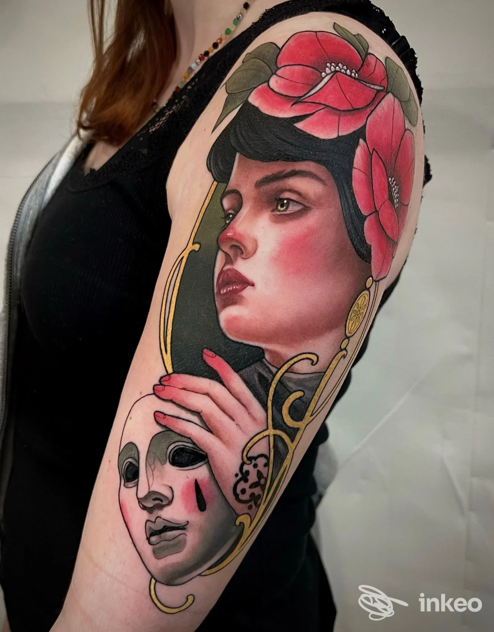 Grande tatuaggio su braccio e spalla con ritratto femminile, fiori rossi e maschera; NEST Tattoo Atelier, Piediripa.