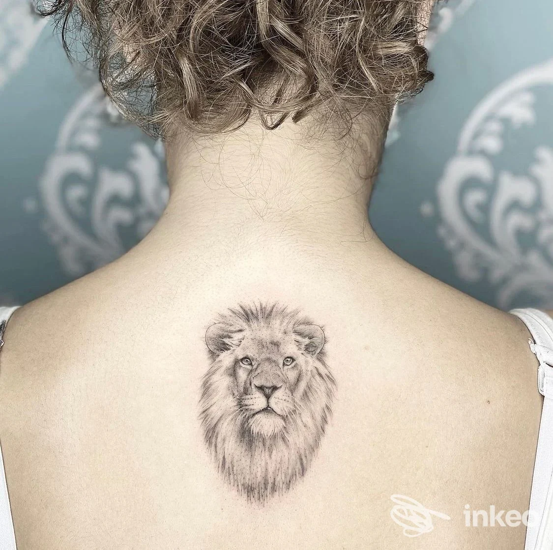Tattoo realistico di un leone sulla schiena di una persona, posizione tra le scapole, visibile in primo piano contro una pelle chiara.
