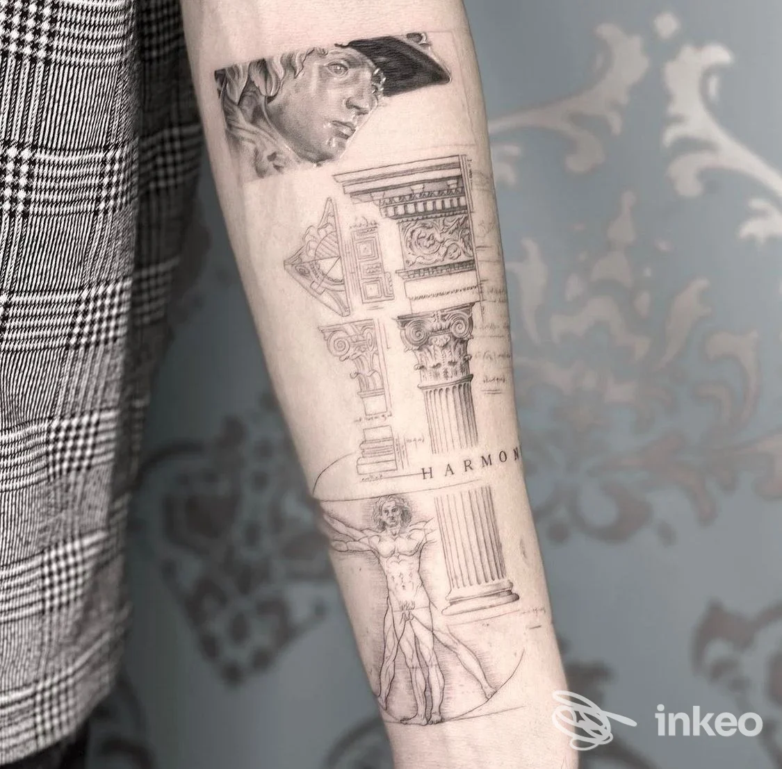Avambraccio con tatuaggi di colonne architettoniche e figura umana, realizzazione corporea visibile senza volto.